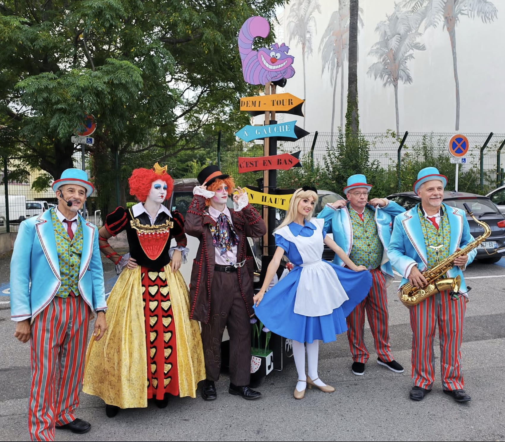 Groupe de personnes déguisées en personnages de conte de fées, avec un panneau coloré indiquant «Demi-tour» à «Gauche» et «C'est en bas» ainsi que des adultes habillés en costumes de cirque ou de clown.