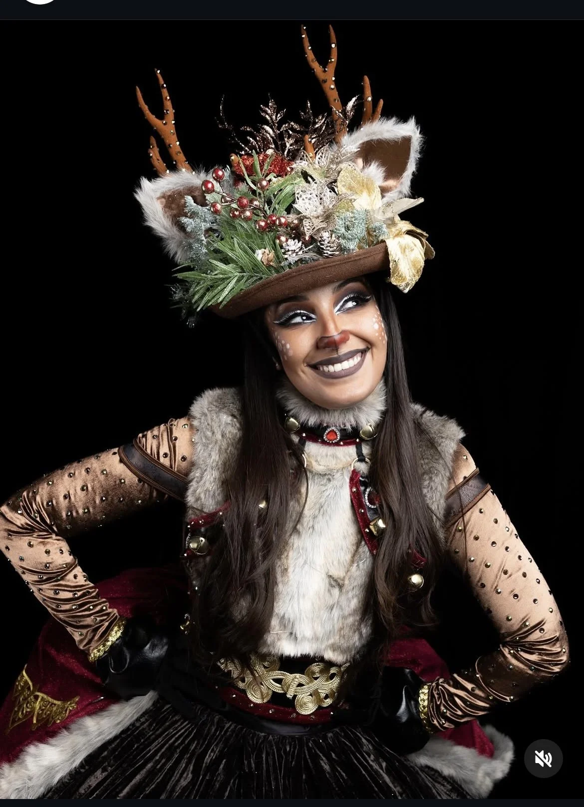 Une femme habillée en costume féerique ou elfique avec un chapeau orné de décorations de Noël, comme des branches, des baies rouges, et des éléments naturels. Elle porte un maquillage élaboré, avec des motifs faciaux et un sourire.
