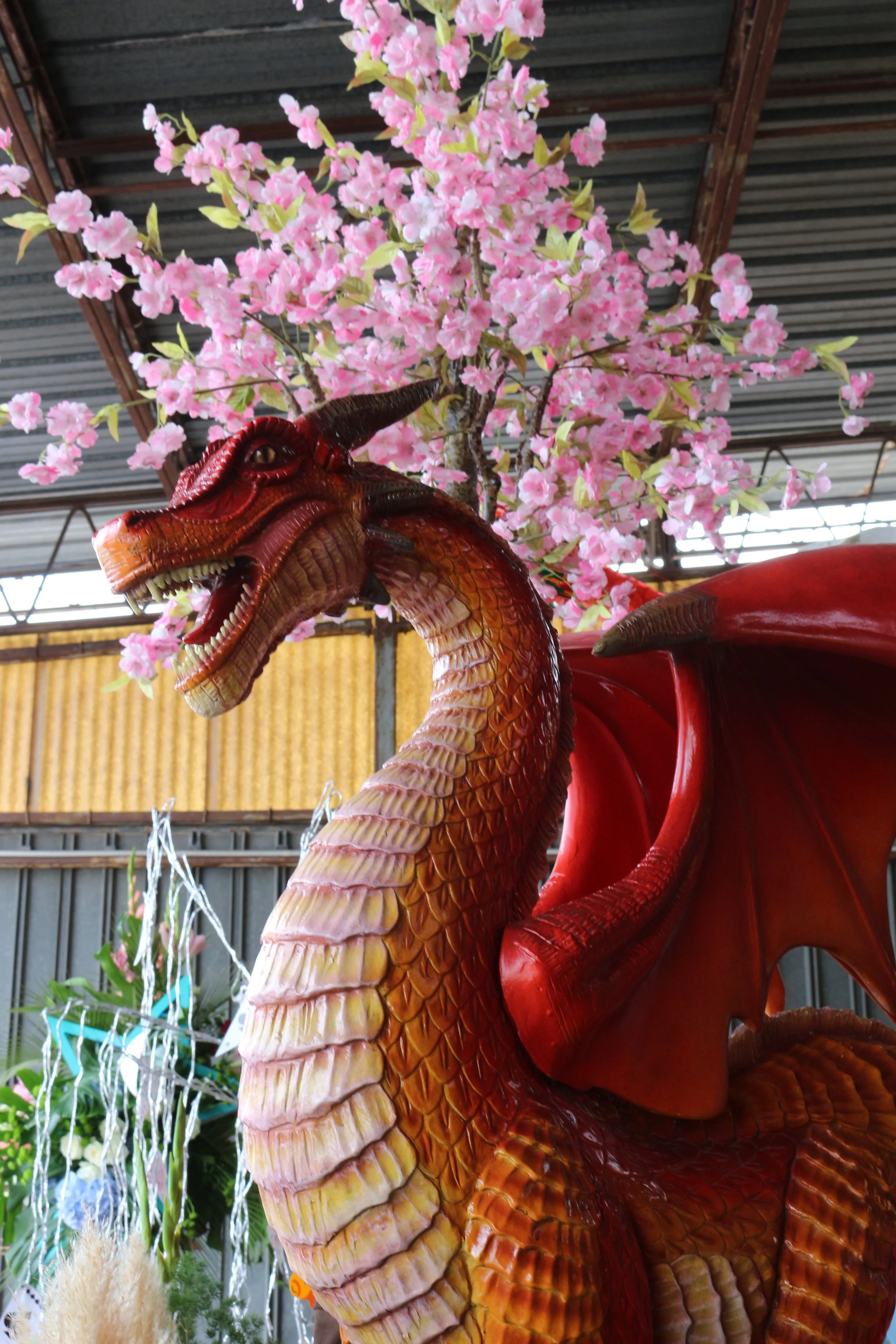 Une statue de dragon rouge avec des fleurs de cerisier roses en arrière-plan.