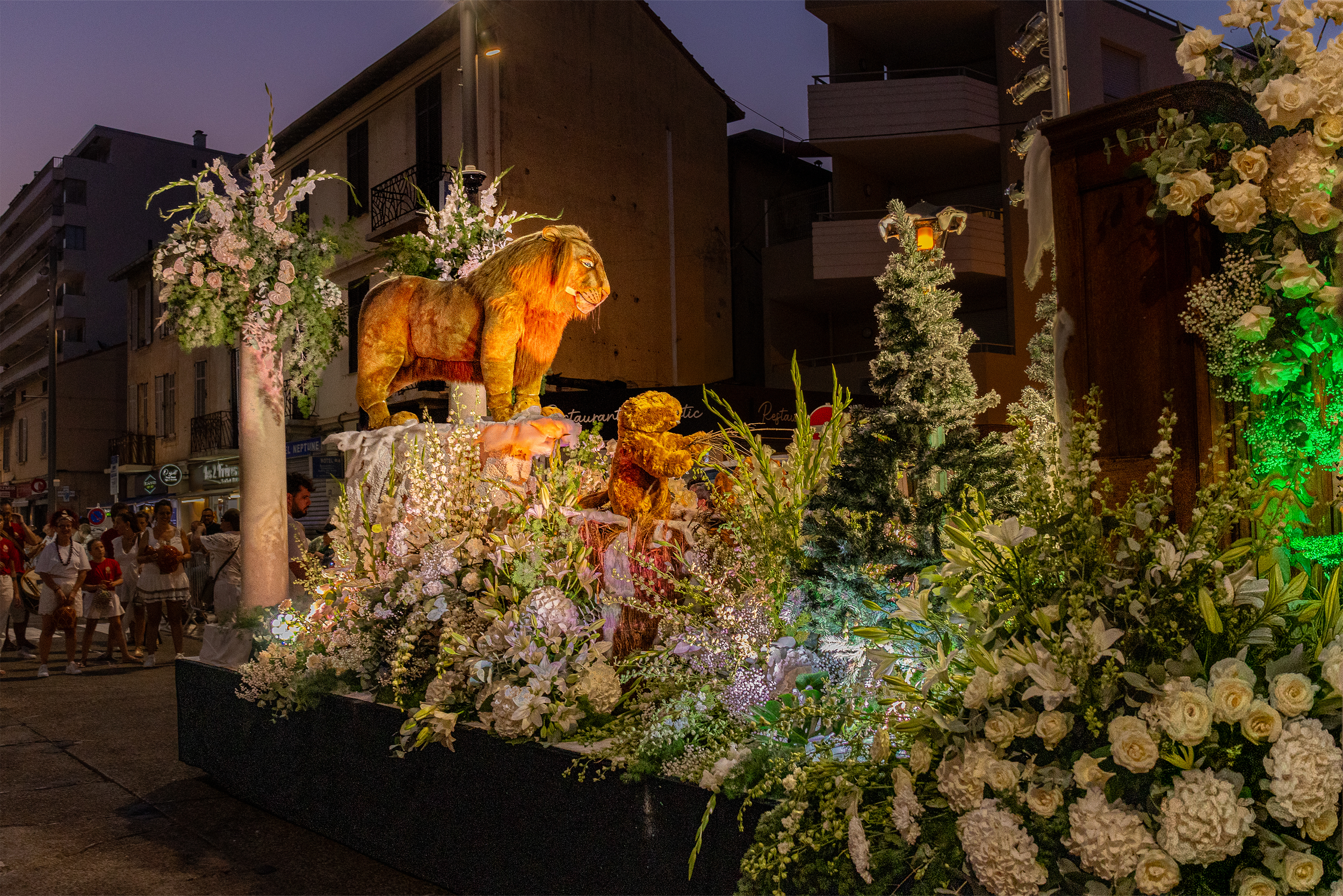 Un char décoré de fleurs et une statue d'un lion dans une procession de parade nocturne