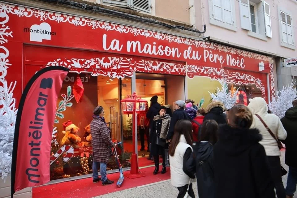 Des personnes se tiennent devant un magasin décoré sur le thème des fêtes, appelé « la maison du Père Noël », avec des décorations et des sapins de Noël.