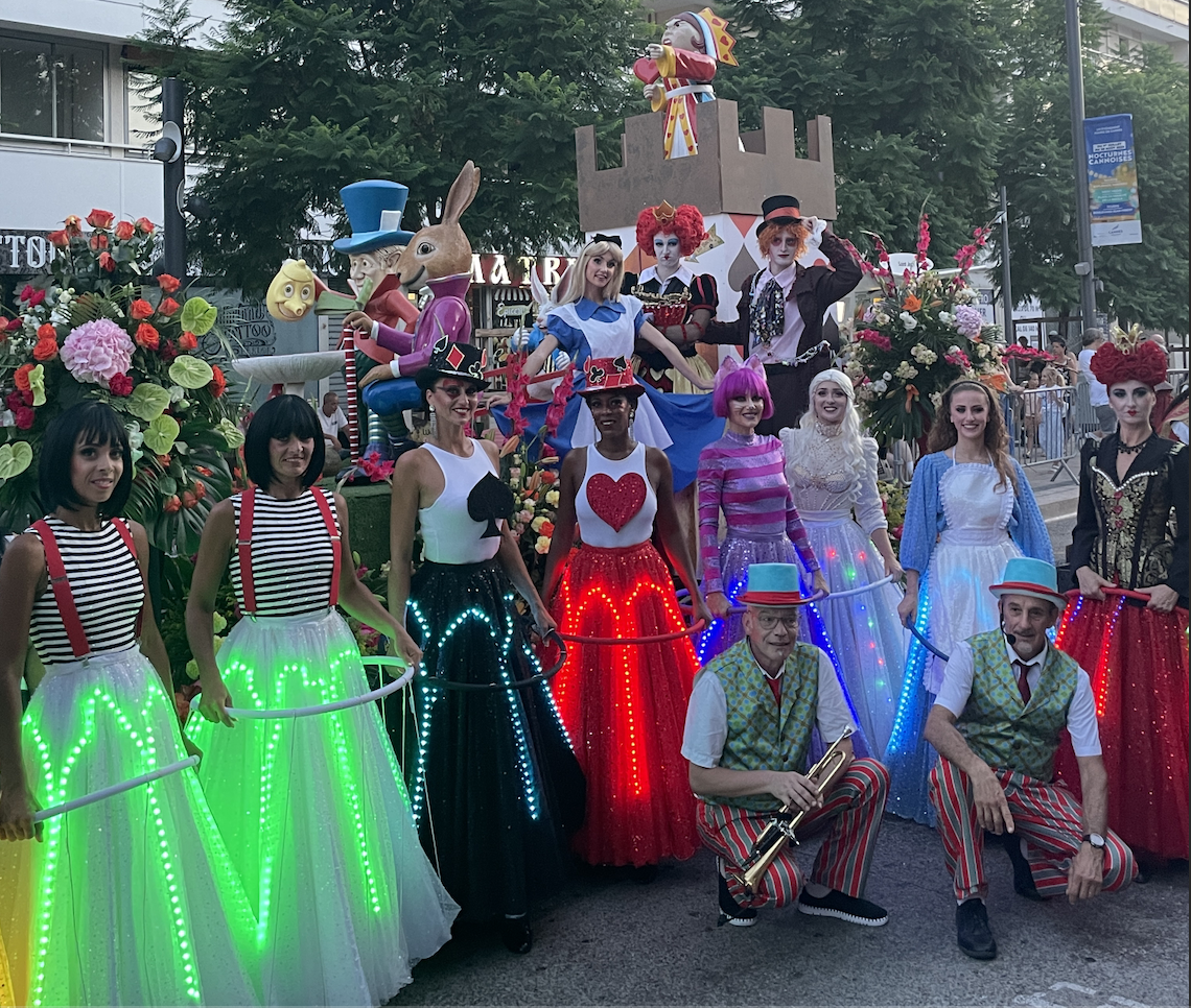 Groupe de personnes déguisées en personnages de conte de fées, avec des costumes colorés et des décorations florales, lors d'une parade ou d'un spectacle en plein air.