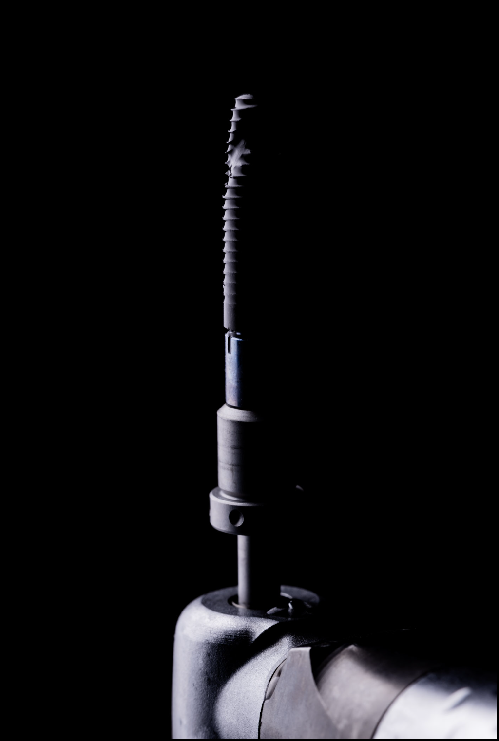 Close-up of a medical robotic arm with a surgical drill attached, illuminated against a black background.