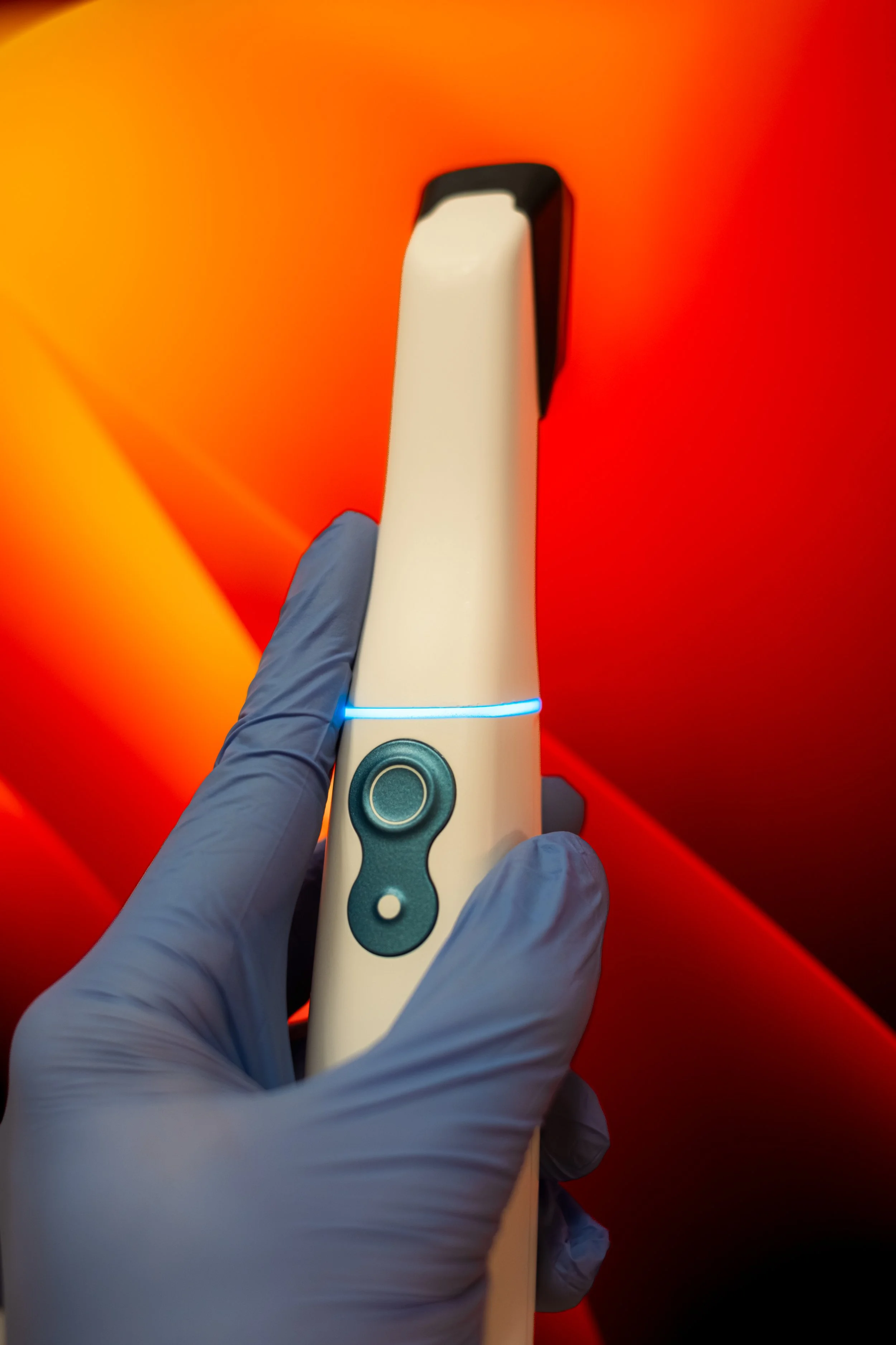 A gloved hand holding a medical device with a glowing blue LED, with a red background.