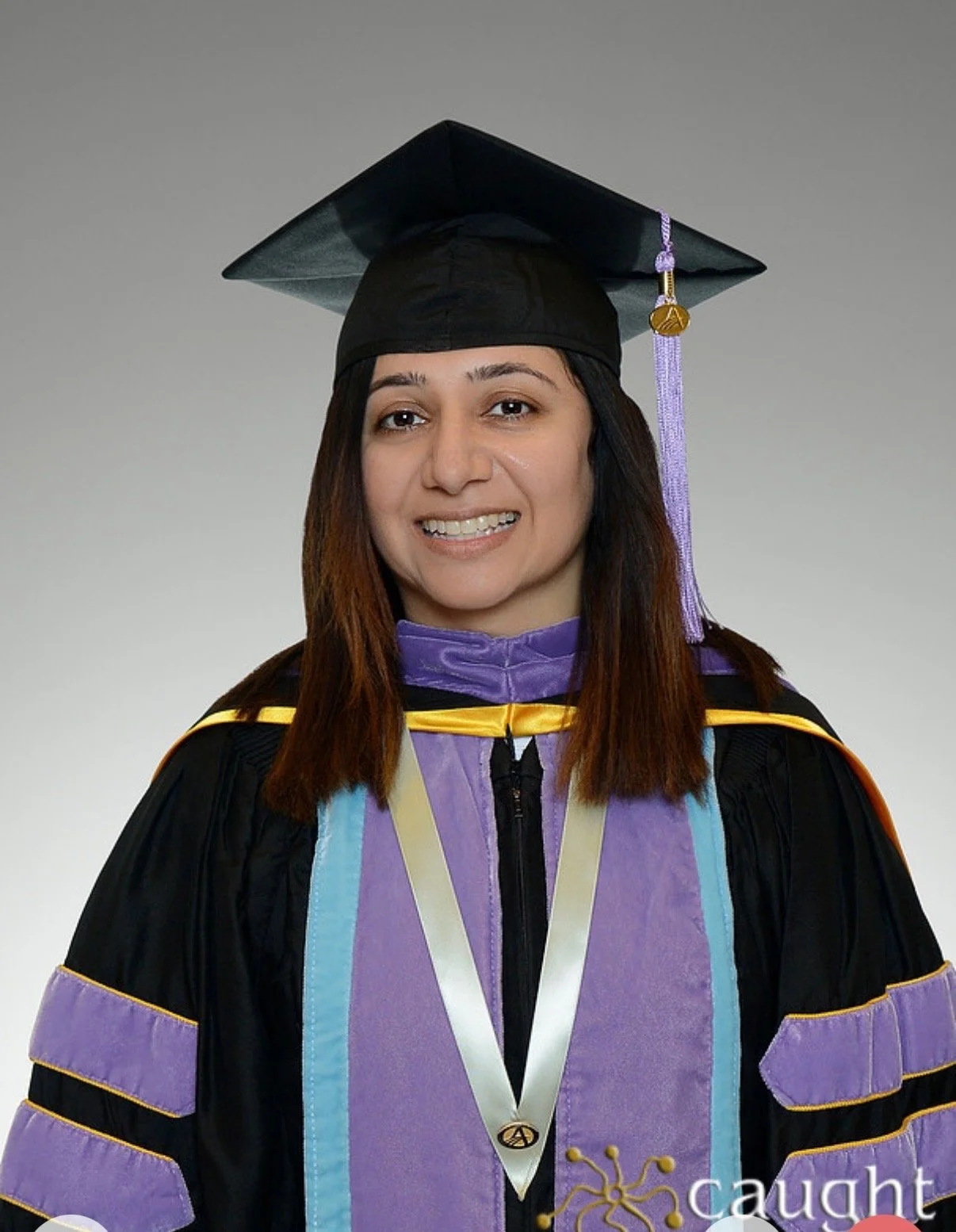 A woman in graduation regalia, including a cap and gown, smiling at the camera.