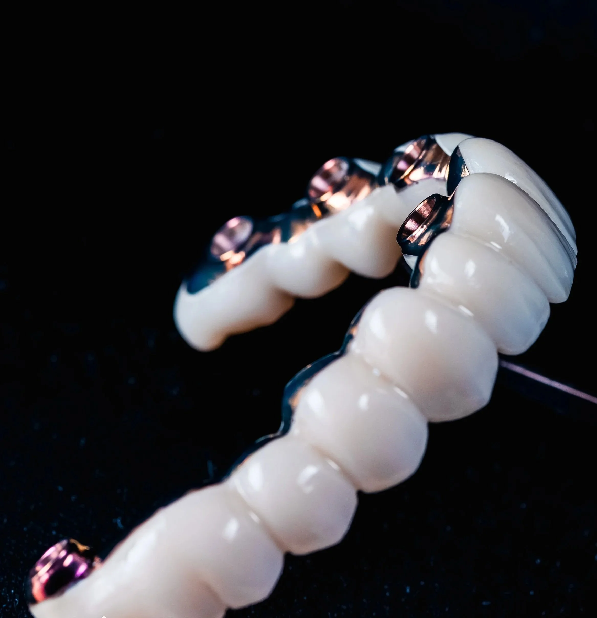 Close-up of a white and pink metallic object with rounded shapes, against a black background.