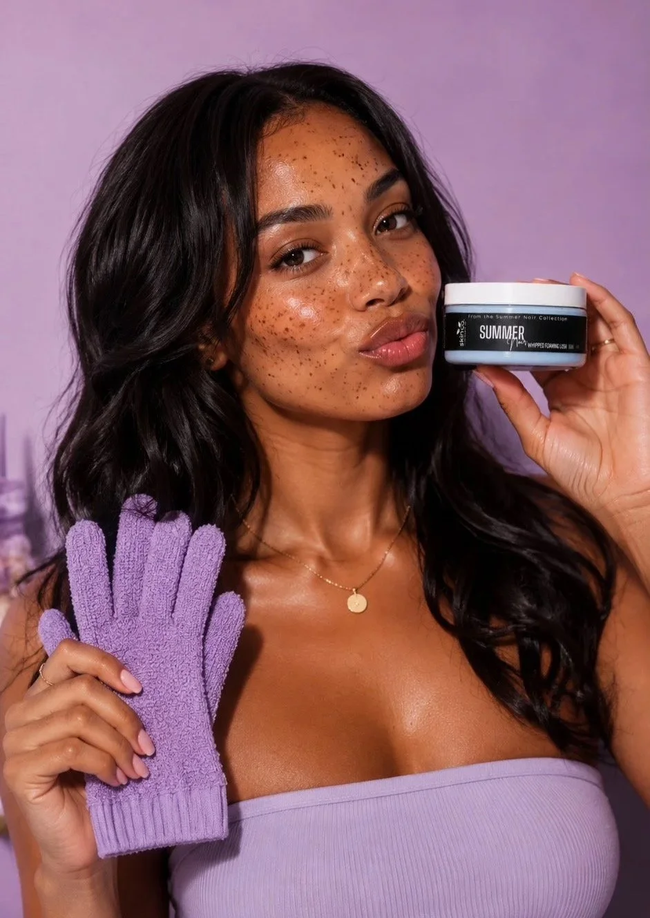 A woman holding a Summer Noir body care product against a purple backdrop.