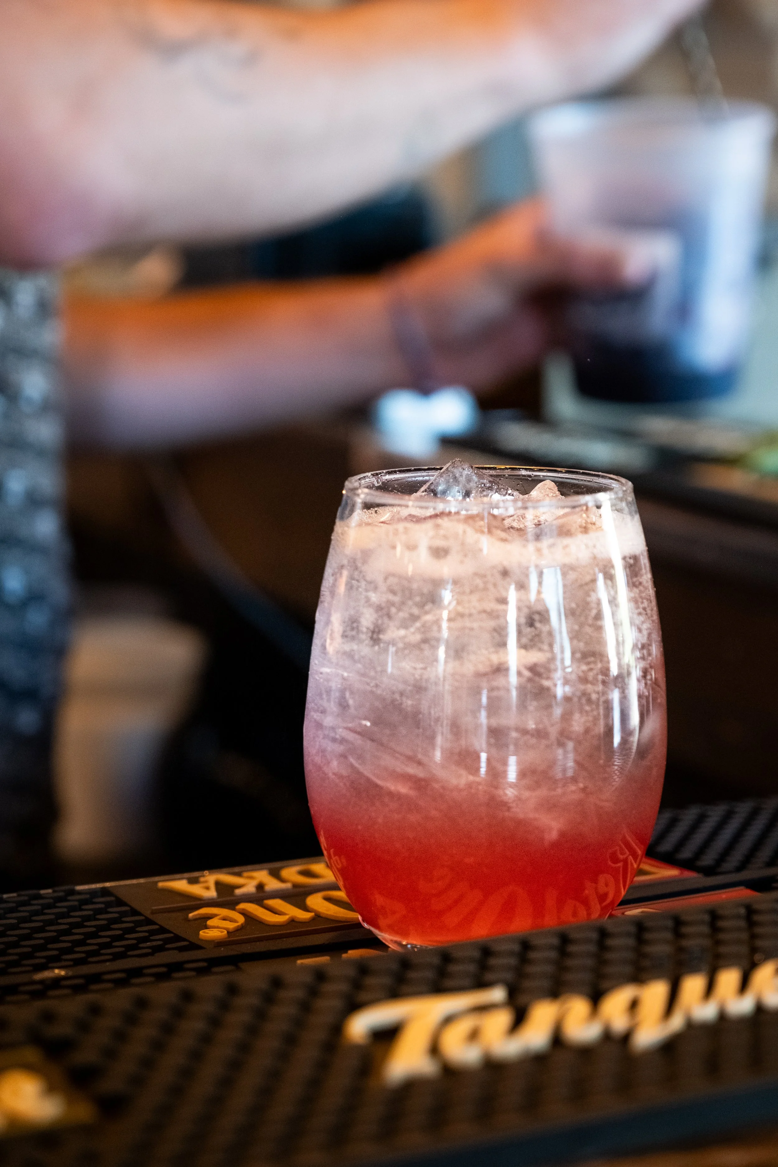 A pink-colored cocktail with ice cubes on a bar counter.