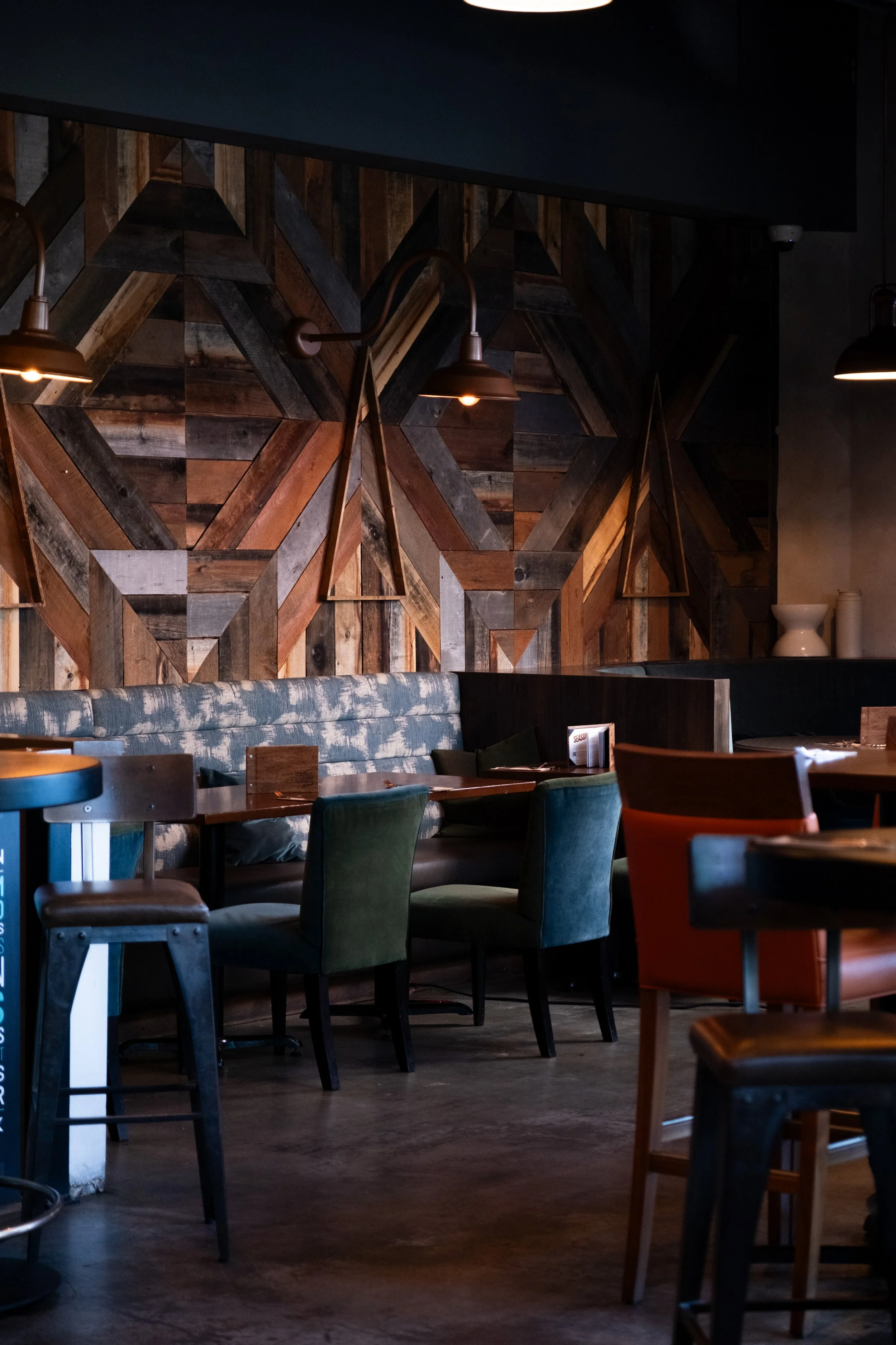 Interior of a rustic restaurant with wooden wall art, upholstered chairs, and dim lighting.