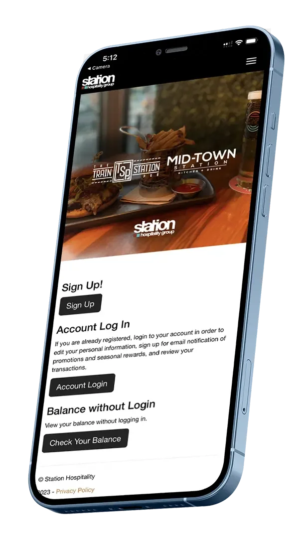 Smartphone displaying login and sign-up options for Station Hospitality Group app, with a background image of food and drinks at Mid-Town Station restaurant.