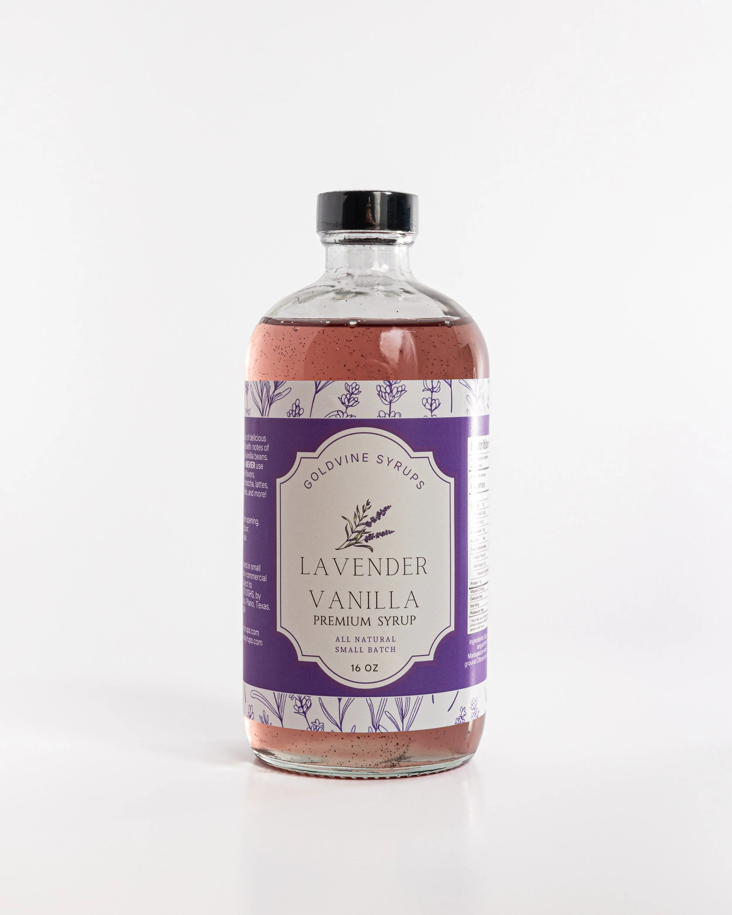 A clear glass bottle of lavender vanilla syrup with a black cap and a purple and white label featuring illustrations of lavender flowers.