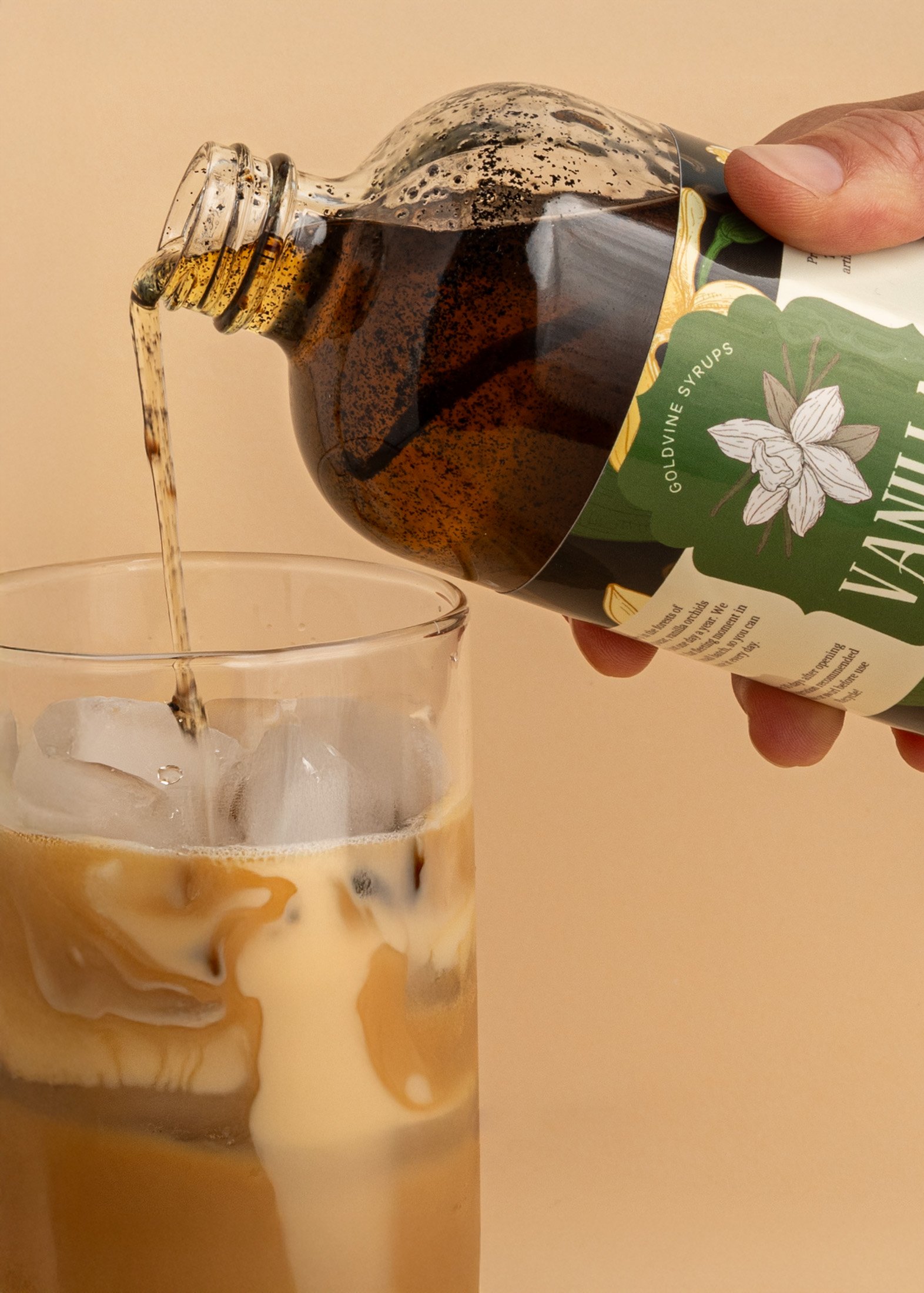 Person pouring syrup into a glass of iced coffee with milk.