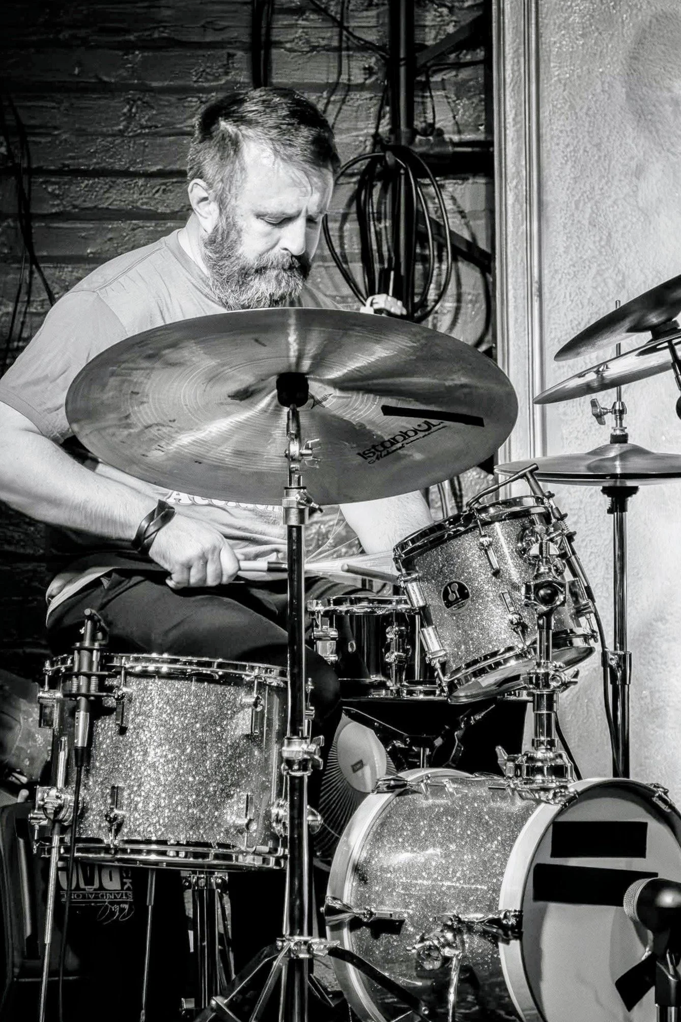 A man with a beard playing a drum set in a music studio.