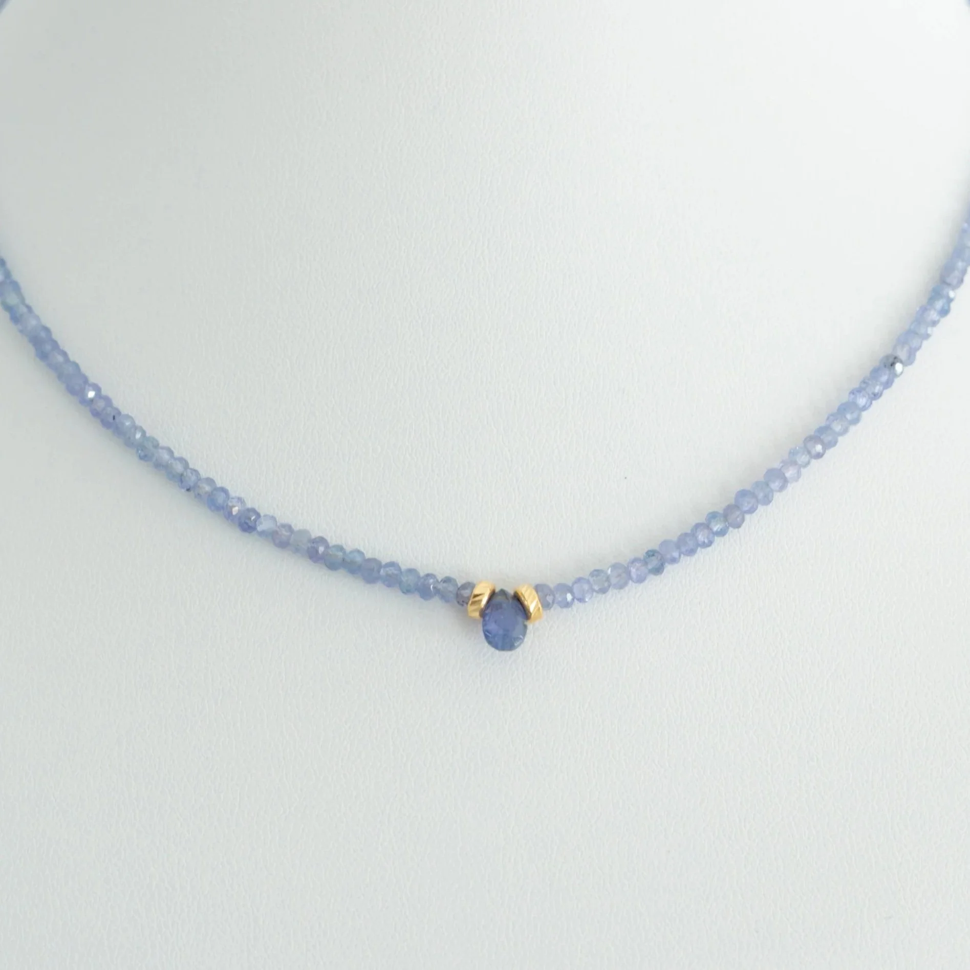 A delicate necklace with purple beads and a central purple gemstone pendant, accented by gold-colored details.