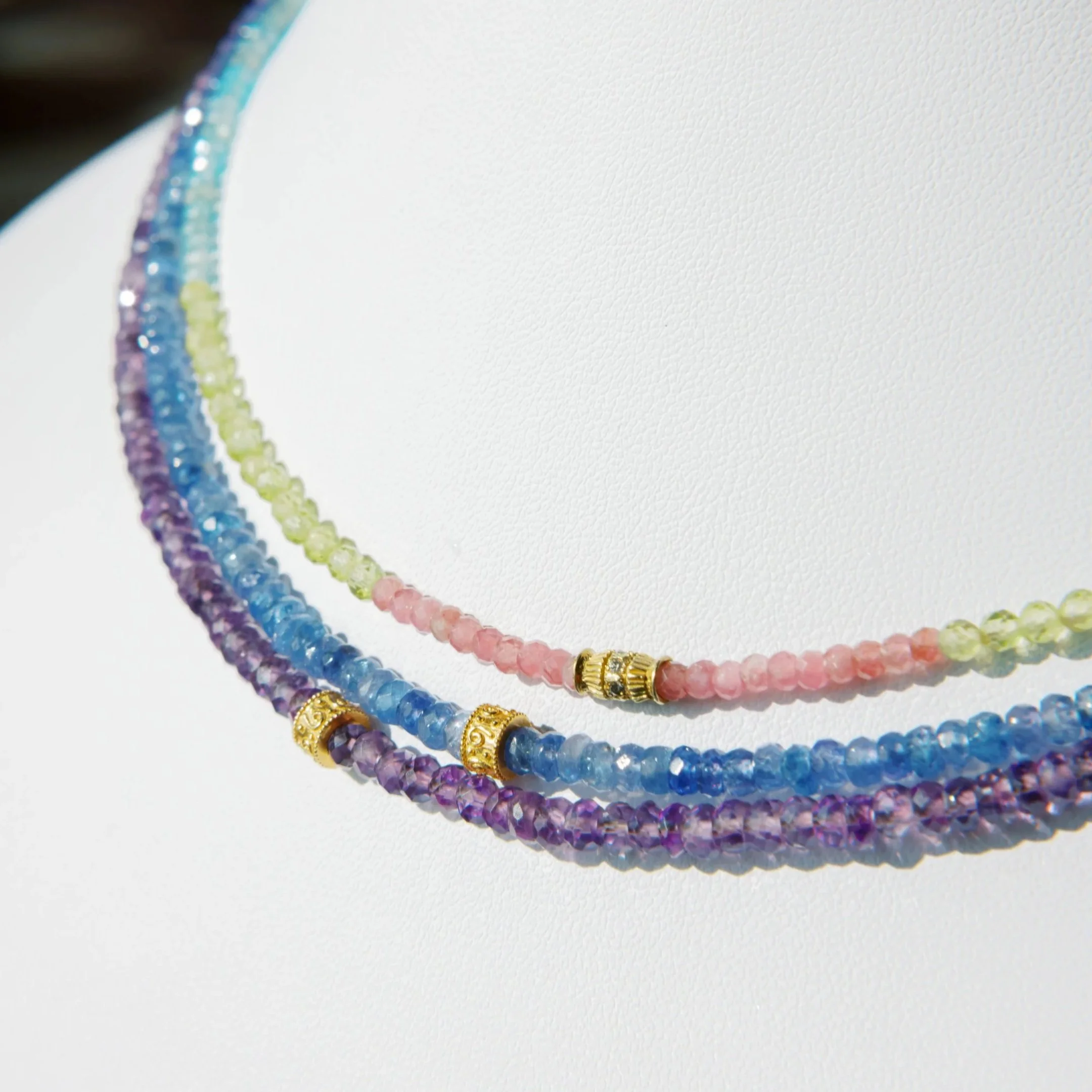 Several colorful beaded necklaces with gold accents lying on a white surface.