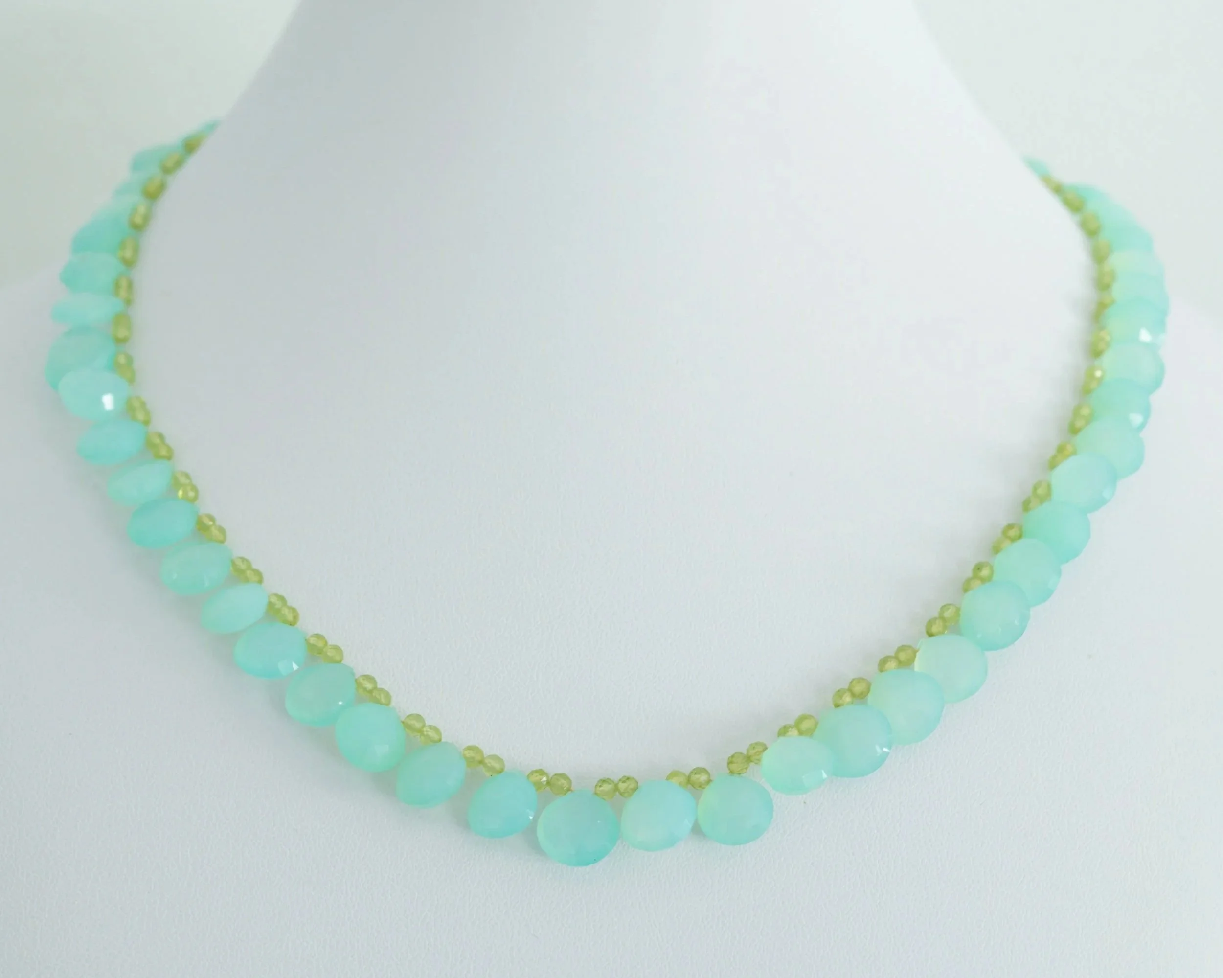 Close-up of a turquoise and light green beaded necklace on a white surface.