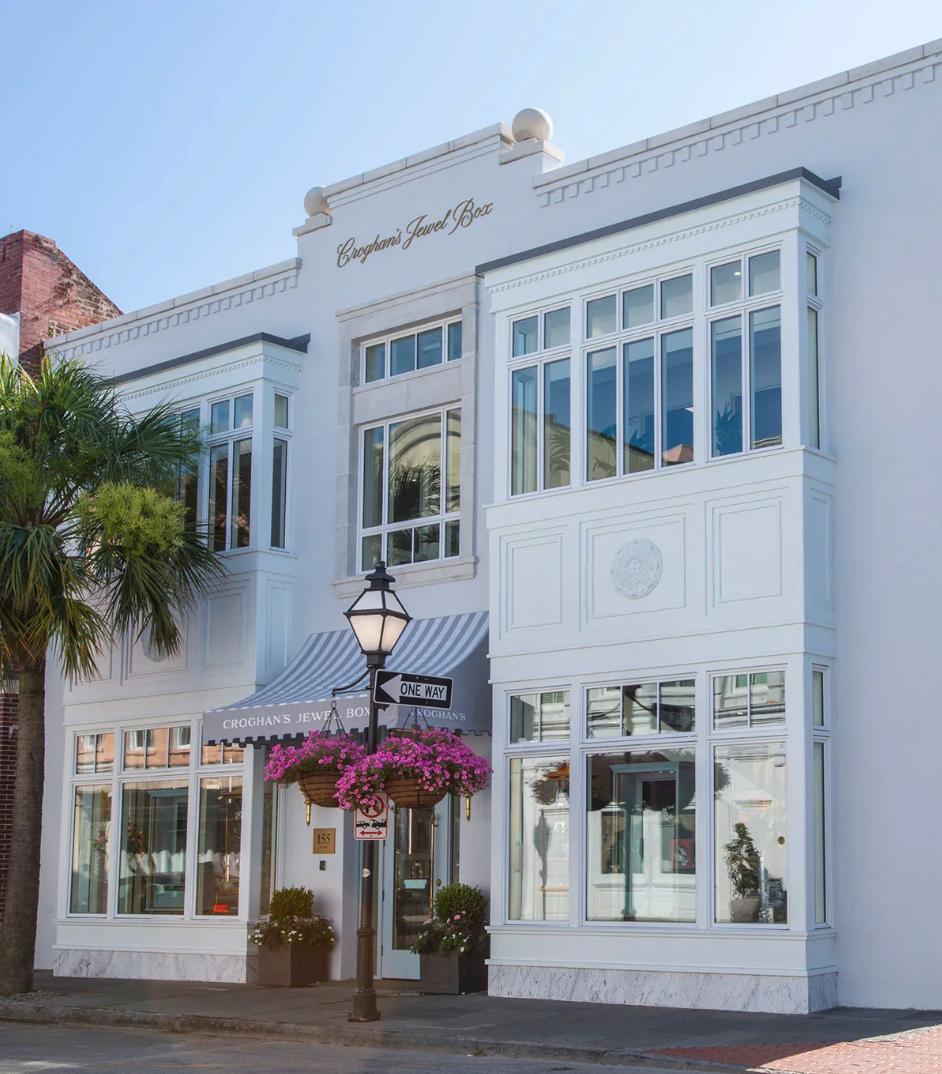 White building with large windows, a striped awning, a street lamp with a hanging basket of pink flowers, a sign reading 'One Way,' and the name 'Croghan's Jewel Box' at the top.