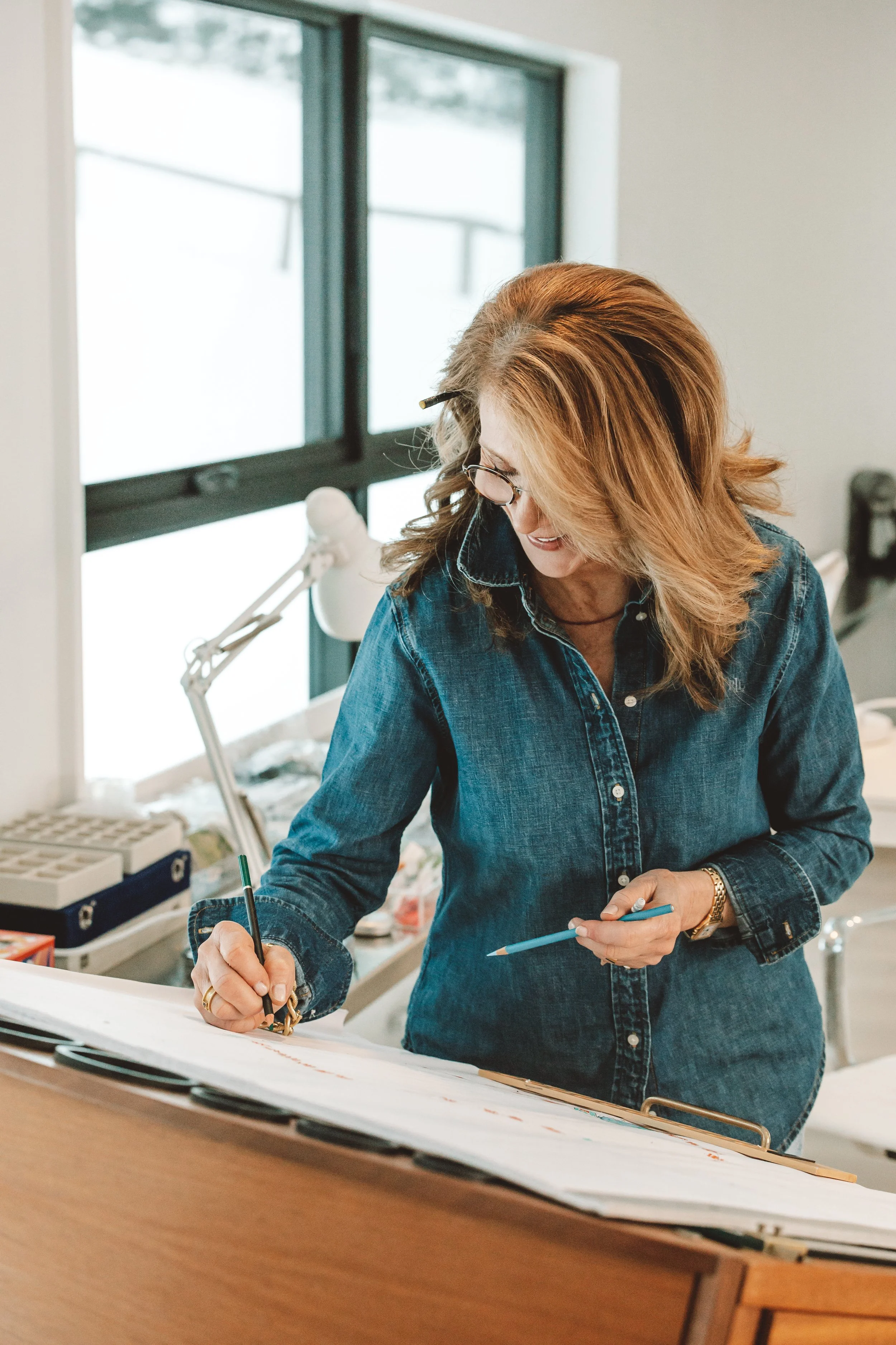 A woman standing at a desk, writing on a large sheet of paper with a black marker.