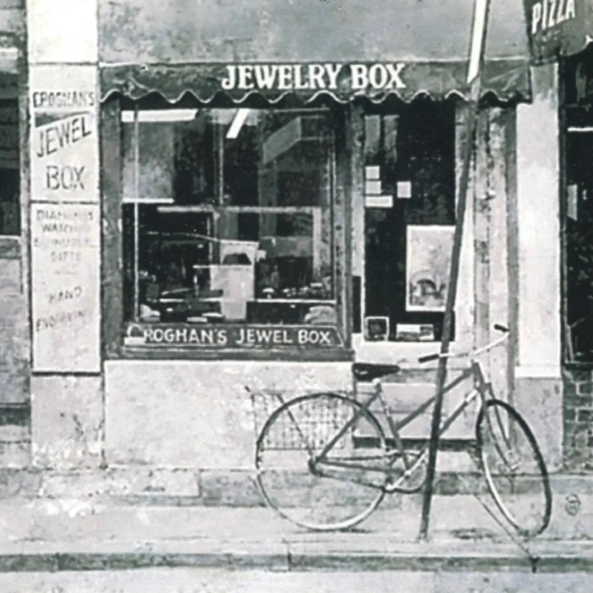Storefront with signs reading "Jewelry Box" and "Fogan's Jewel Box," a bicycle parked outside, and window displays showcasing jewelry items.