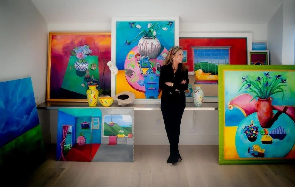 Woman standing in a room filled with colorful abstract paintings on the walls and floor.