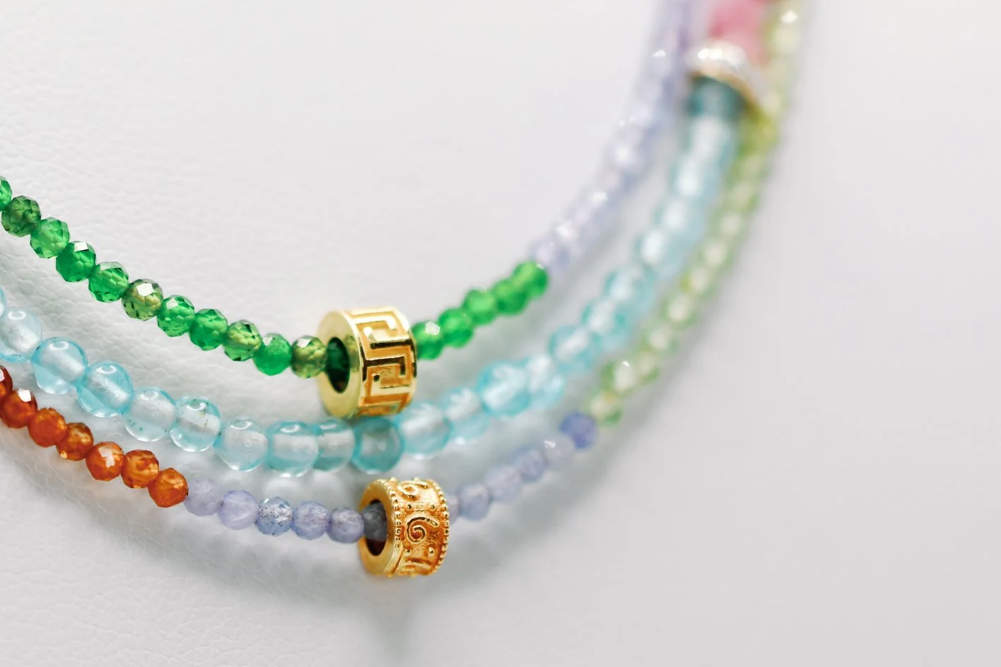 Close-up of colorful beaded necklaces layered on a white surface, with gold decorative spacers.