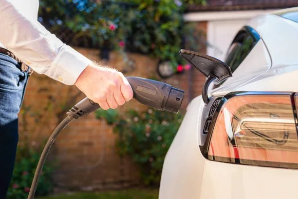 Person charging an electric car with a portable charger outdoors.