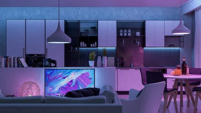 Modern living room and kitchen area illuminated with purple and pink lighting, featuring a sofa, a television, dining table with chairs, and kitchen cabinets with decor