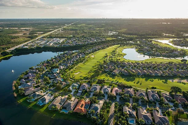Aerial view of a suburban neighborhood with houses, a golf course, and lakes, extending towards the horizon on a clear day.