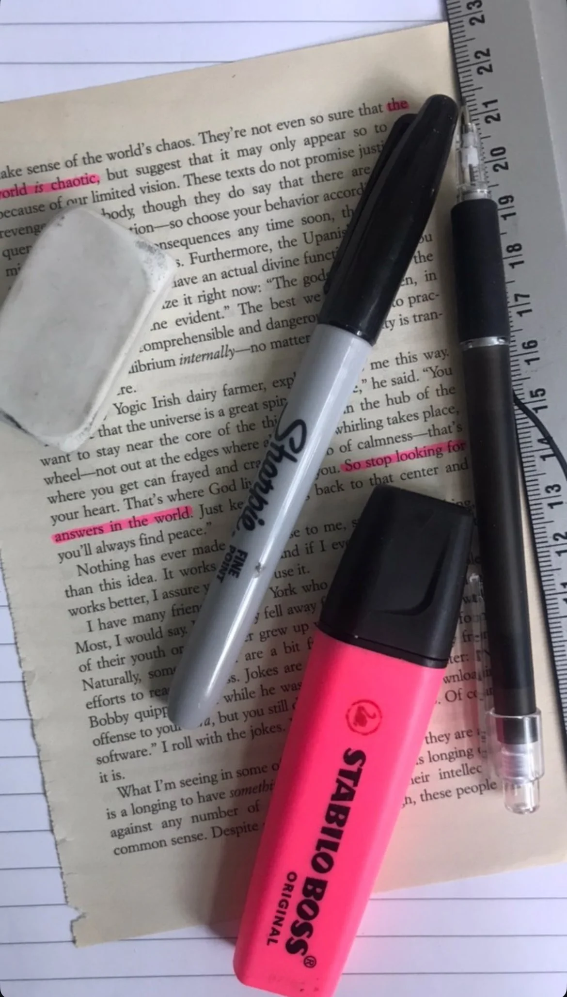 Close-up of a page from a book with a highlighter, a marker, and an eraser on top. The page has highlighted text in pink, with some parts underlined and highlighted.