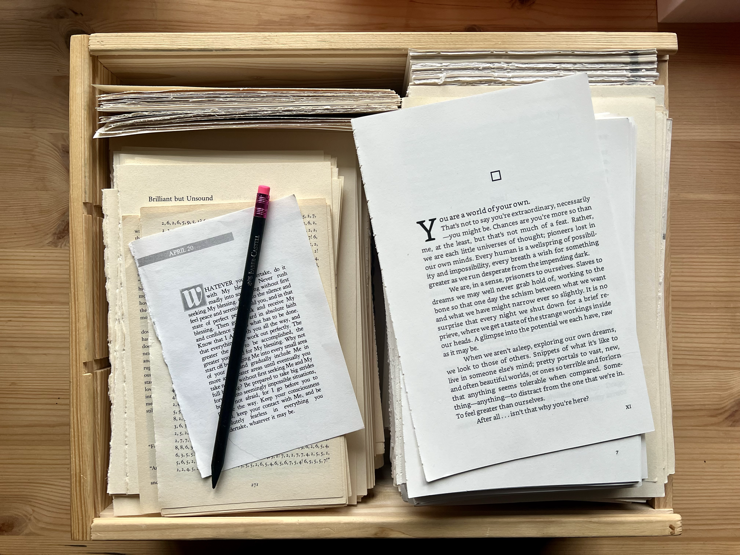 Open book with printed text placed in a wooden box, with a pink and black pen resting on smaller papers, on a wooden surface.