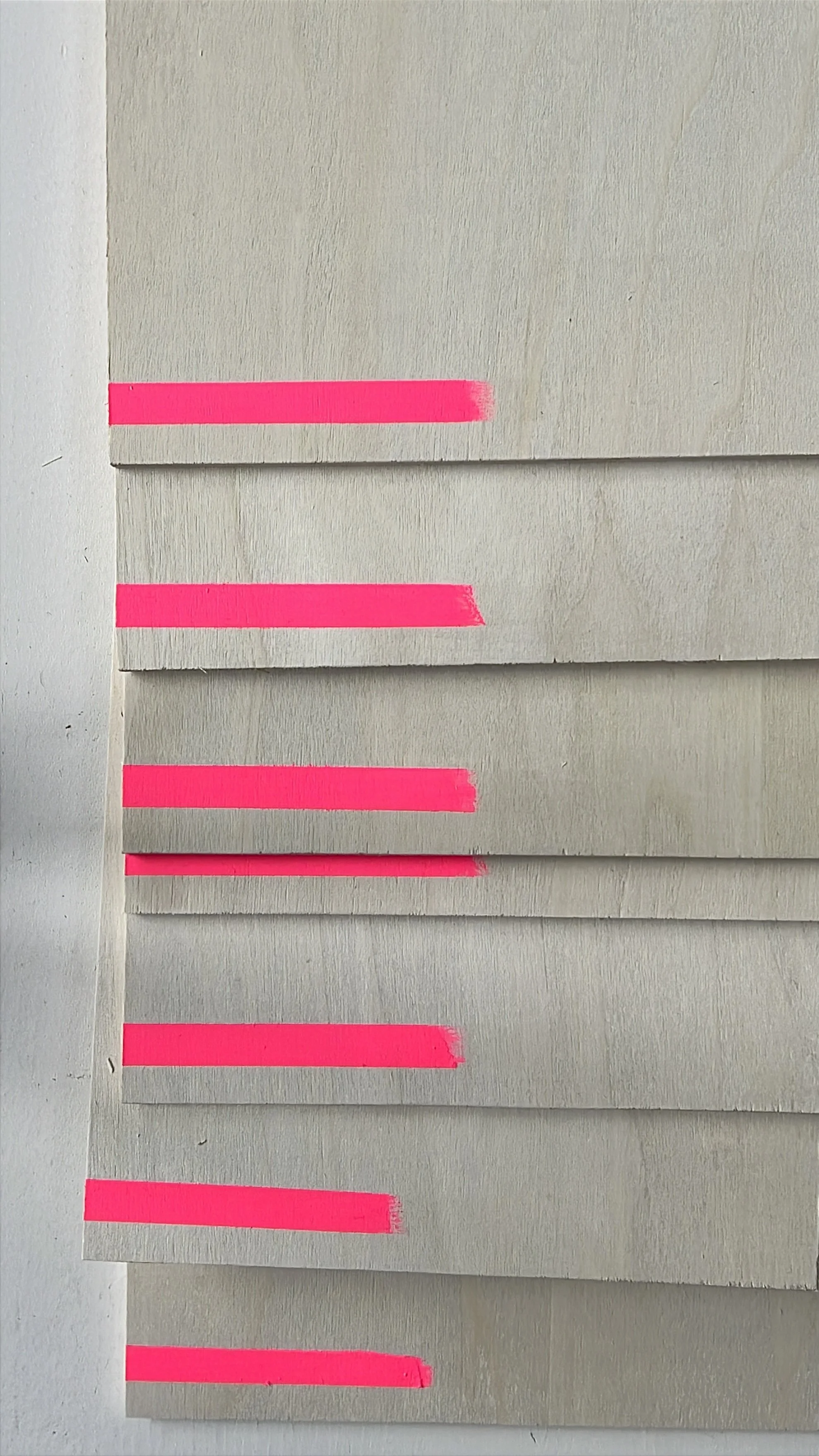 Multiple strips of pink painter's tape on white paper, layered over a beige wall, arranged vertically.