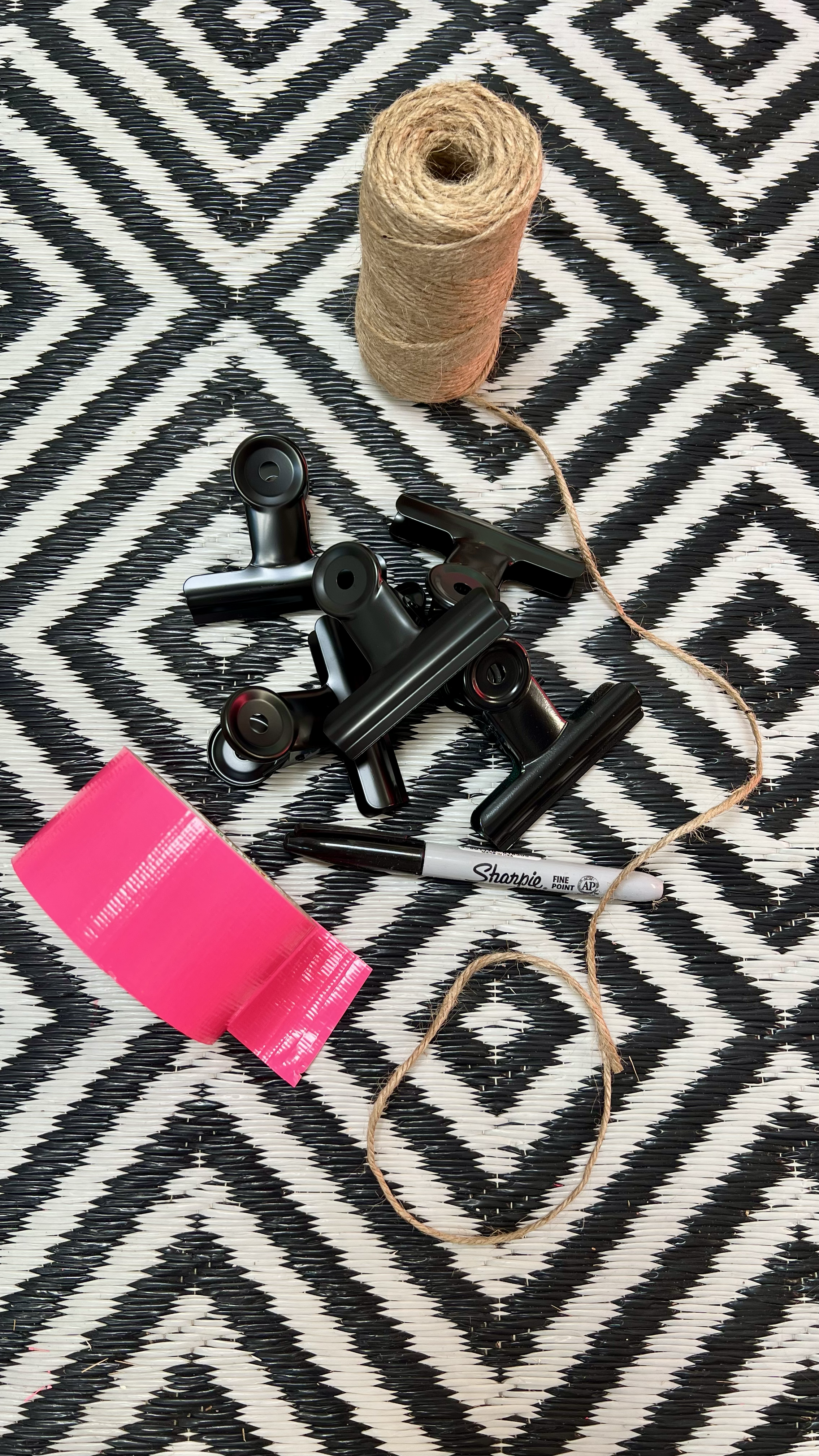 A roll of twine, three black earbuds, a black marker, a pink tape, and a black marker with a white cap are scattered on a black and white patterned surface.