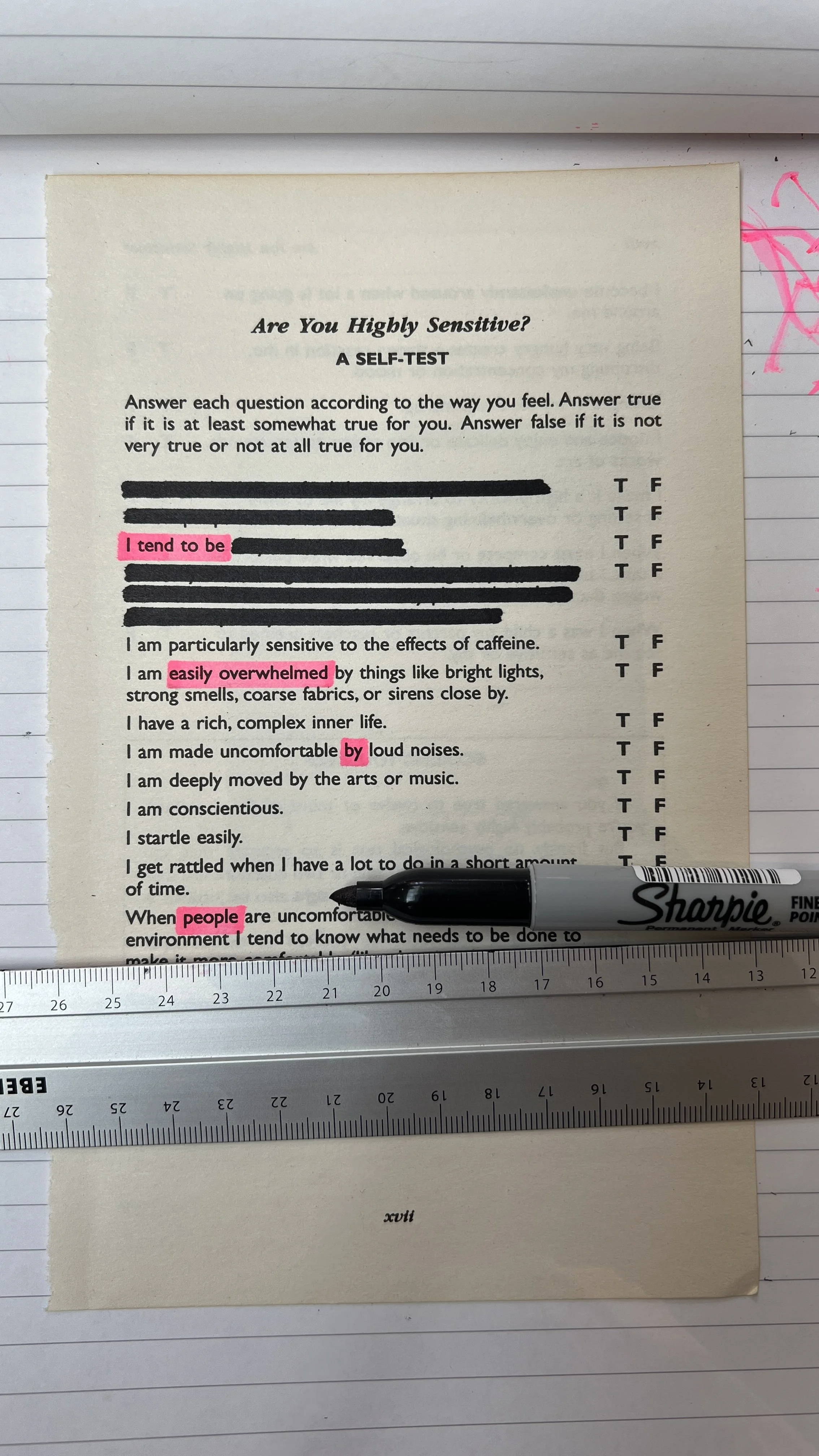 A printed self-test worksheet titled 'Are You Highly Sensitive?' with questions and multiple-choice answers, some options highlighted in pink and marked with a black marker, along with a black Sharpie pen resting on it, placed on a lined sheet of pap