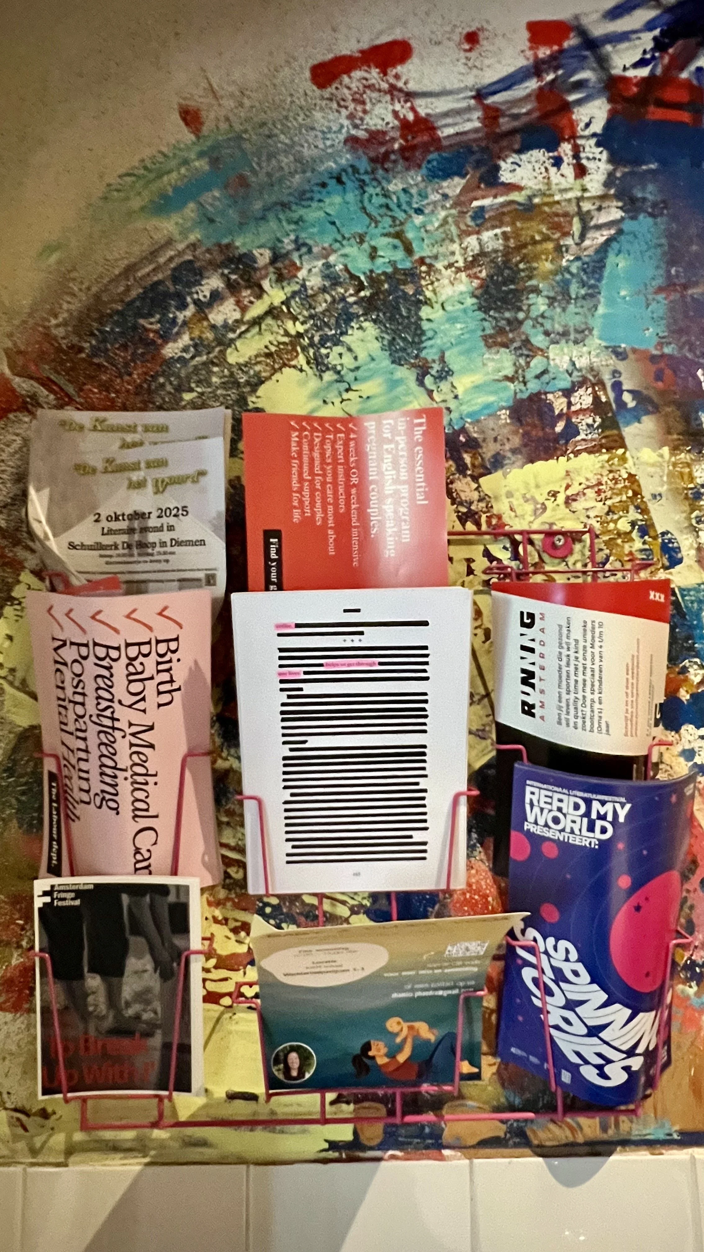 A magazine rack with various magazines and books, including a pink magazine titled 'Birth Baby Medical Card' and a blue bag of Skittles candy.