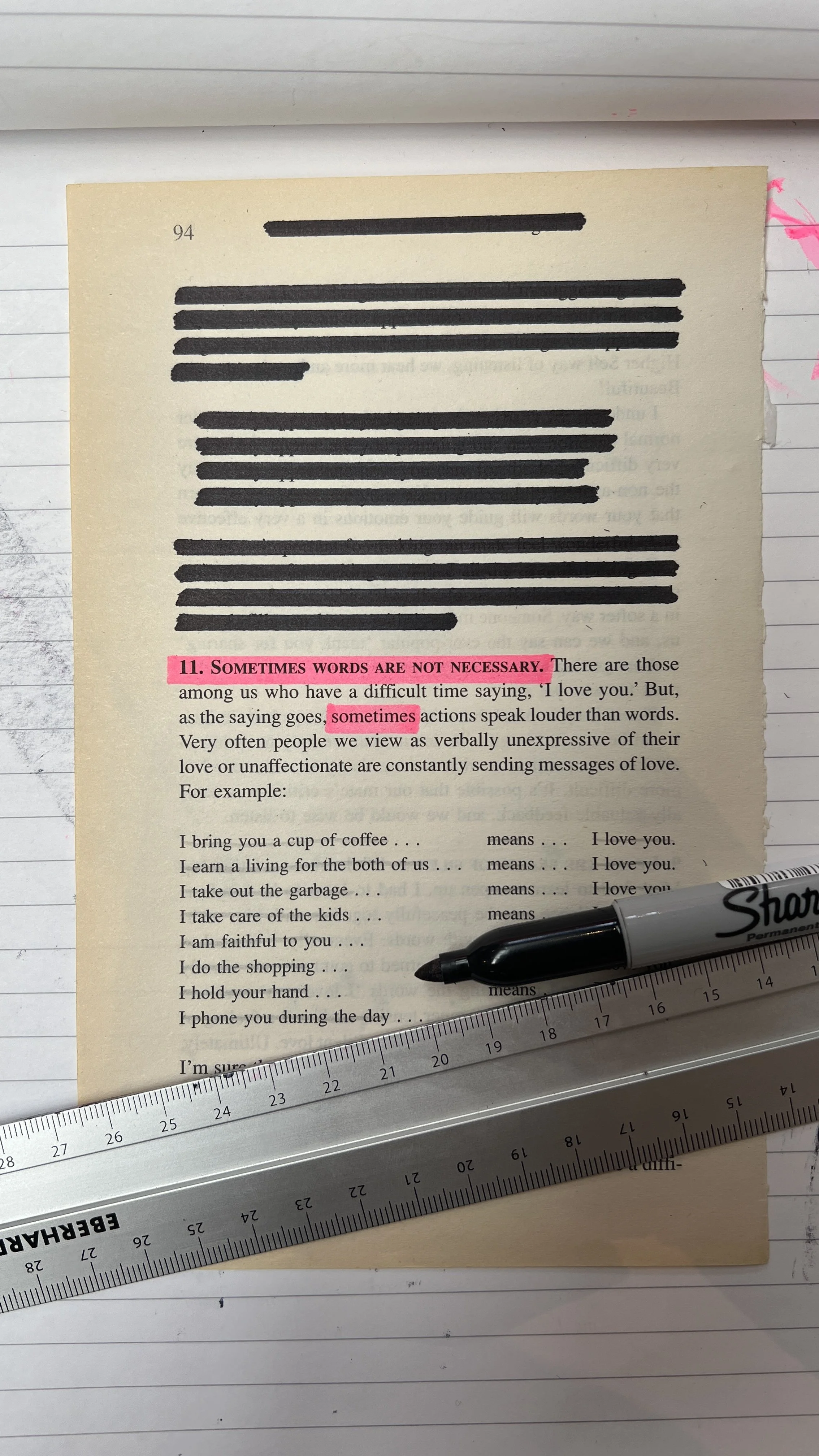 A page from a book with highlighted text, a black marker, and a ruler placed on a lined notebook. The highlighted text reads "SOMETIMES WORDS ARE NOT NECESSARY." and "sometimes". There is pink accent ink on the page. The scene is photographed on a wh