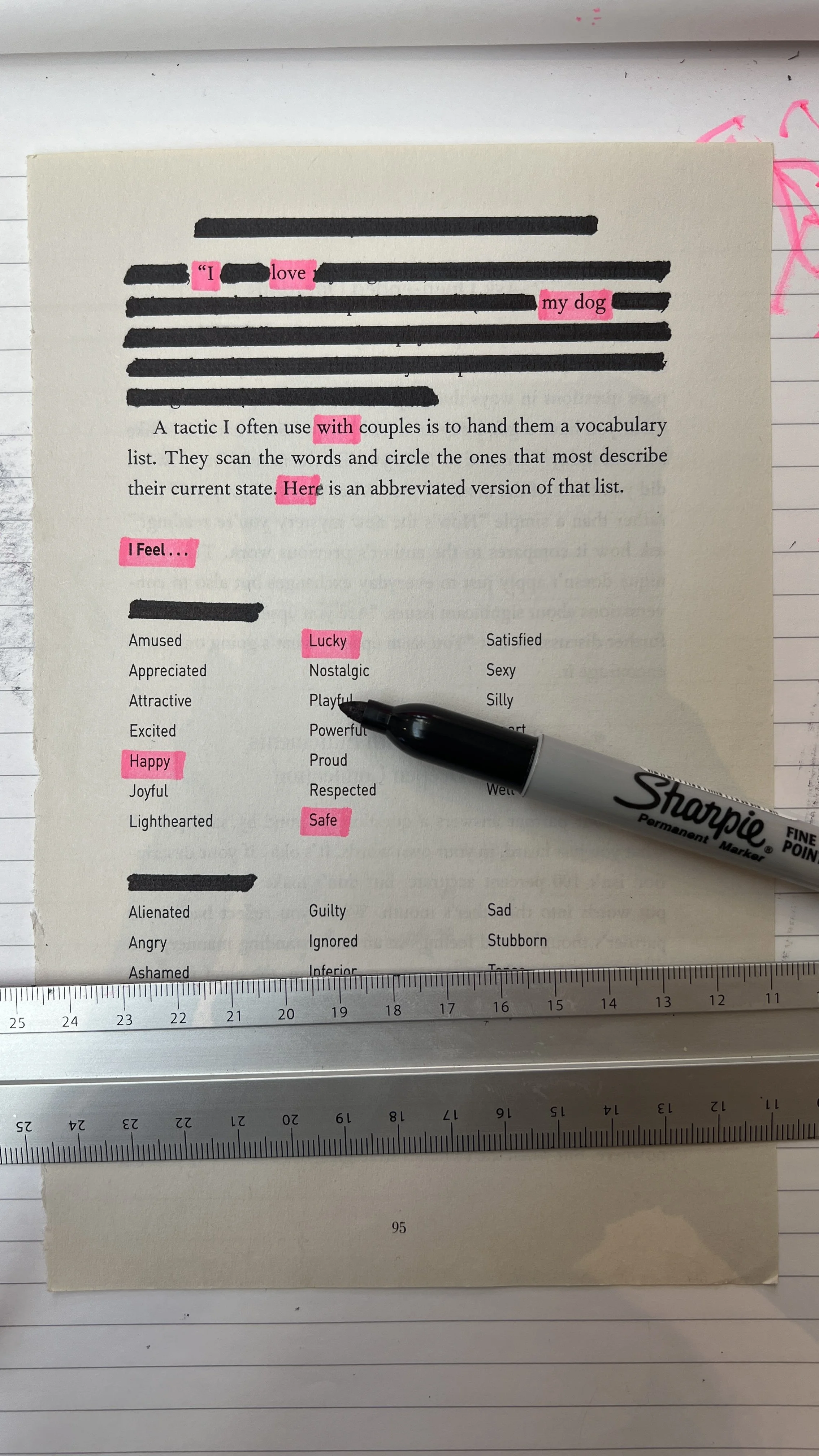 A printed page with handwritten black markings and pink highlighted words, a black marker placed on the page, and a metal ruler at the bottom, all on a lined desk surface.