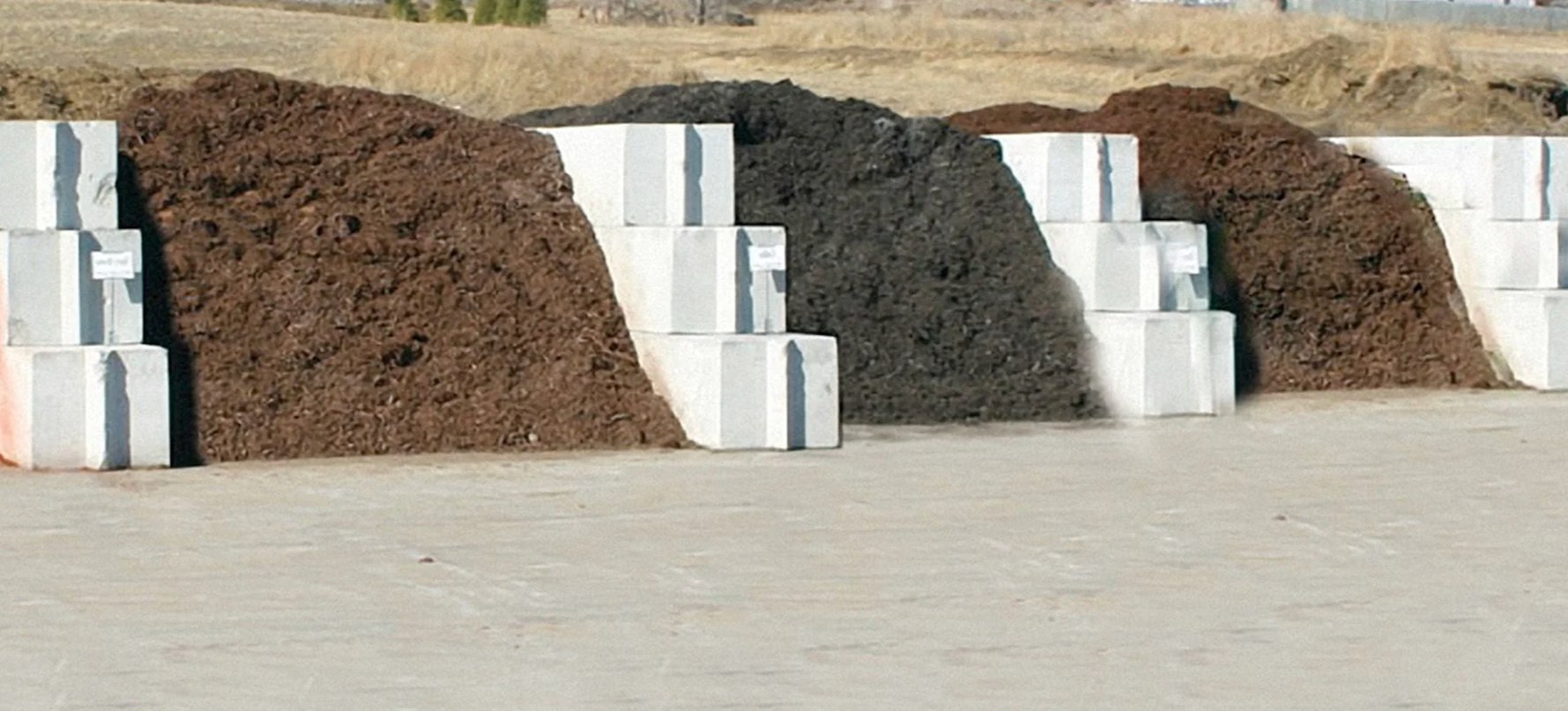 Large piles of dirt or soil in front of white concrete blocks, set outdoors on a flat surface.