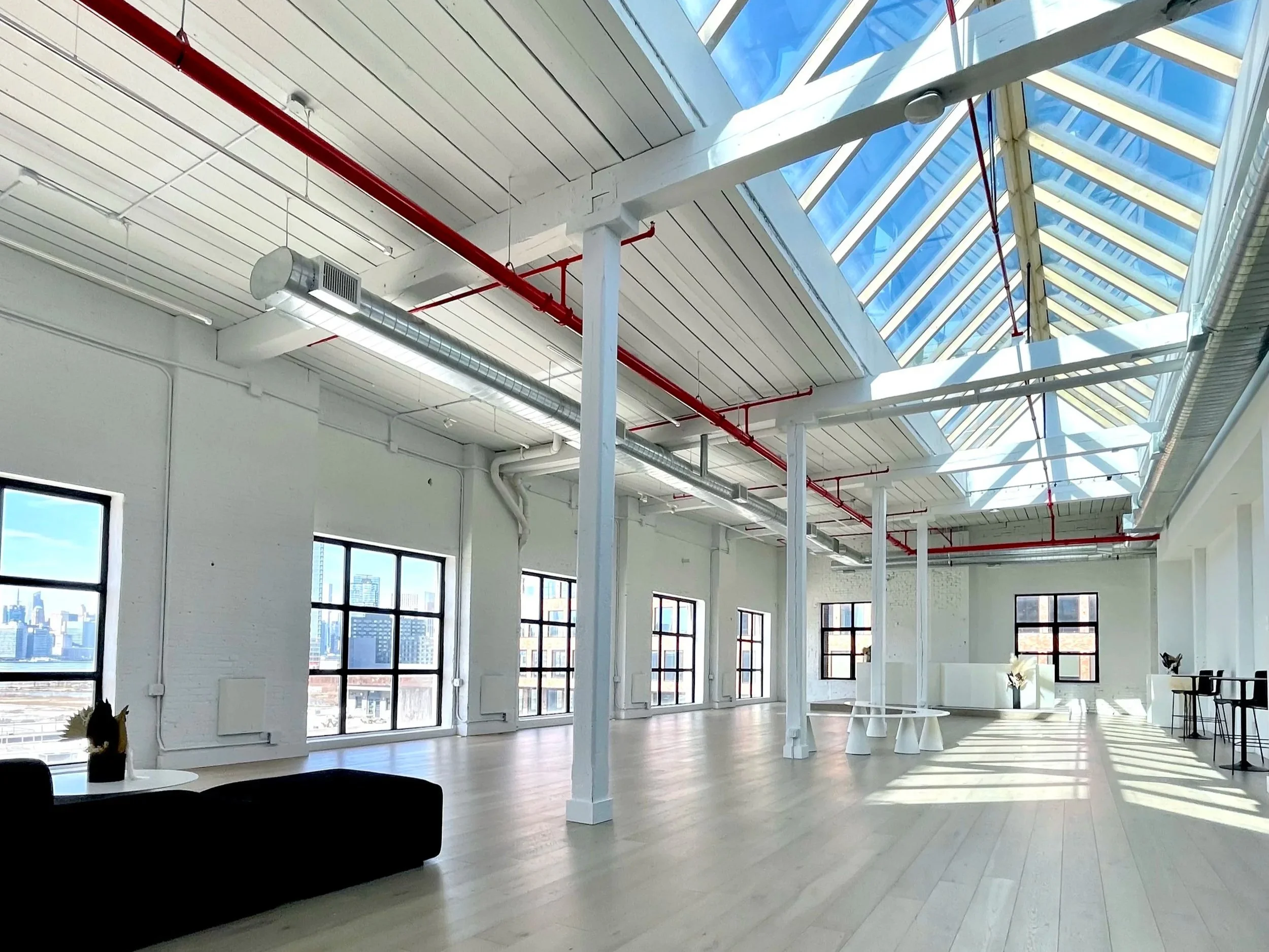 The Brooklyn Rare Book Fair venue: A spacious modern office with large windows, white walls, and high ceilings with skylights. There are minimalistic white tables, chairs, and some potted plants.