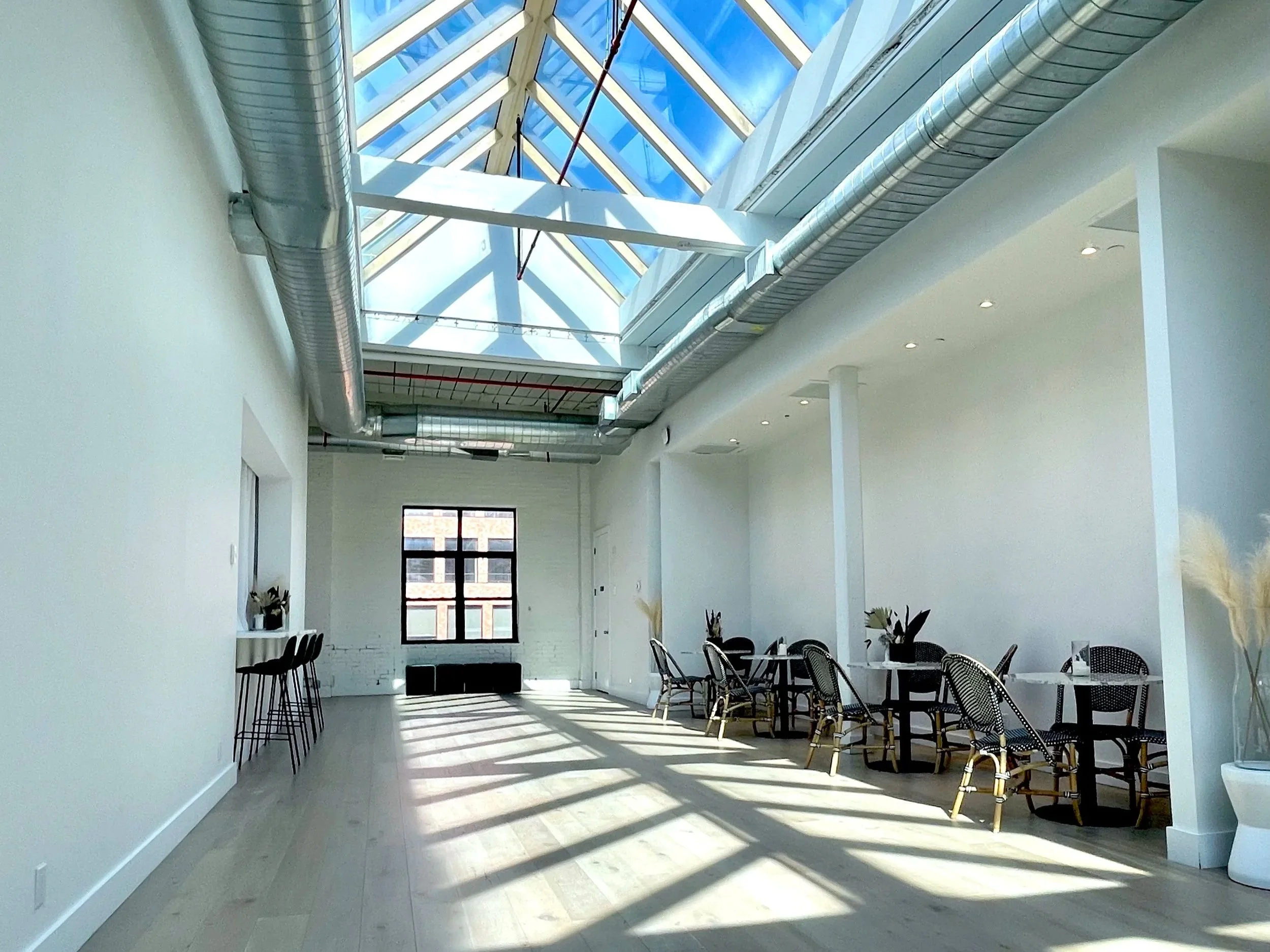 The Brooklyn Rare Book Fair venue: Modern interior space with high glass ceiling, white walls, and black chairs around tables, illuminated by natural sunlight.