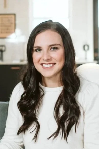 Coach Kayci with long, wavy dark hair smiling in an indoor setting, wearing a white top.