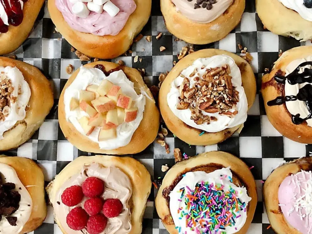 Assorted mini donuts topped with various frostings and sprinkles, arranged on a checkered surface.