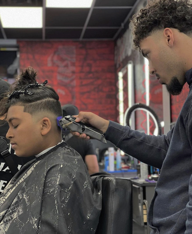 Barber cutting a young man's hair with clippers in a barber shop.