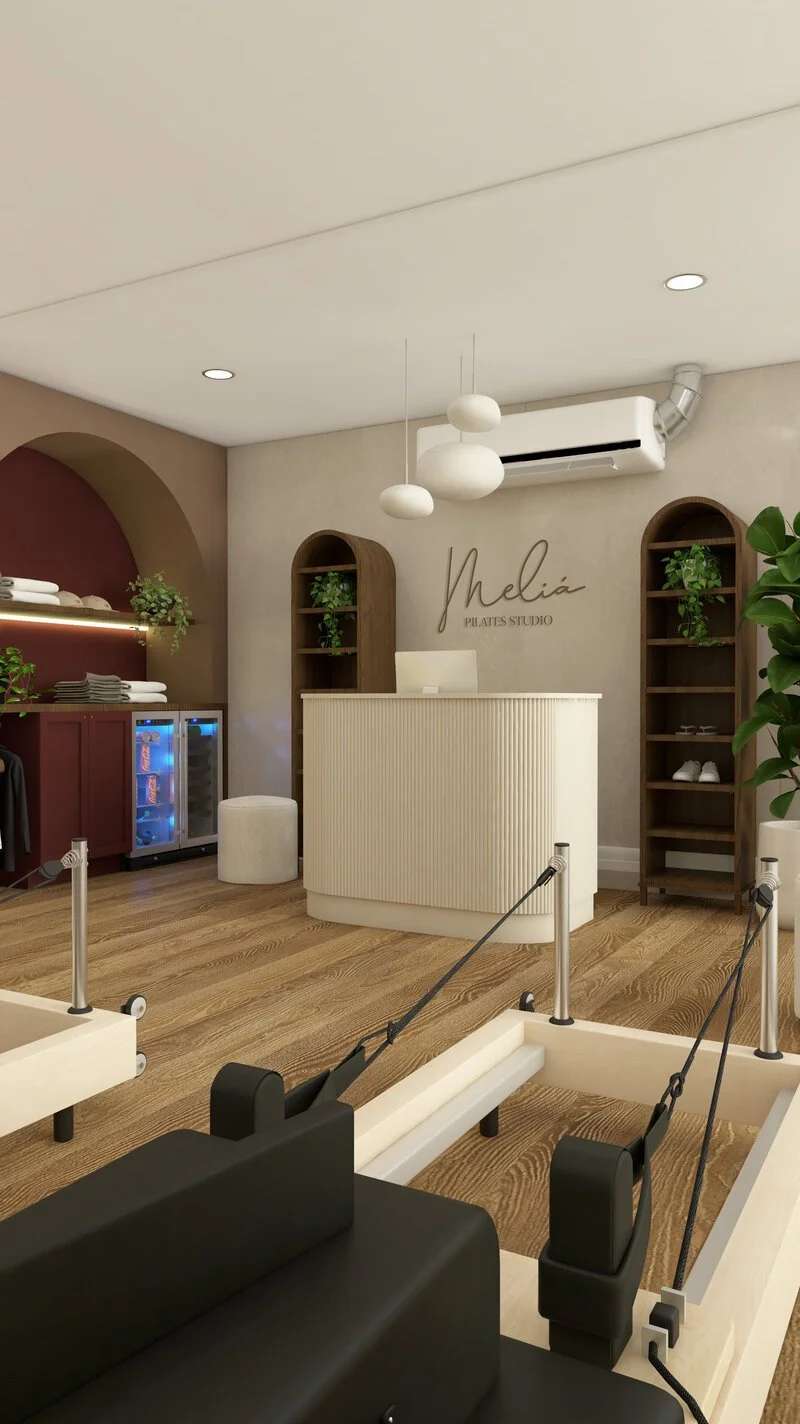 Interior of a Pilates studio with a reception desk, shelves with plants and shoes, a mini fridge, and Pilates reformer machines.