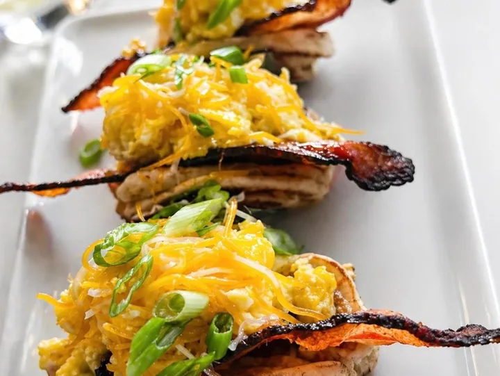 Three servings of appetizers topped with shredded cheese, chopped green onions, bacon strips, and diced eggs on a white rectangular plate.