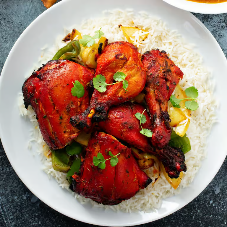 Plate of grilled chicken drumsticks with rice and vegetables garnished with cilantro.
