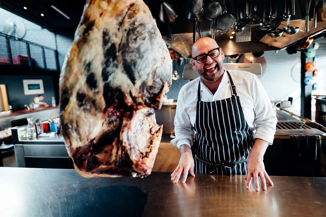 Thomas A. Imbsuch vor einem großen Stück rohem Fleisch in einer modernen Küche.