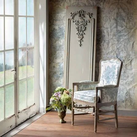 Vintage armchair with floral upholstery next to a window and a flower arrangement on the floor in a decorated room.