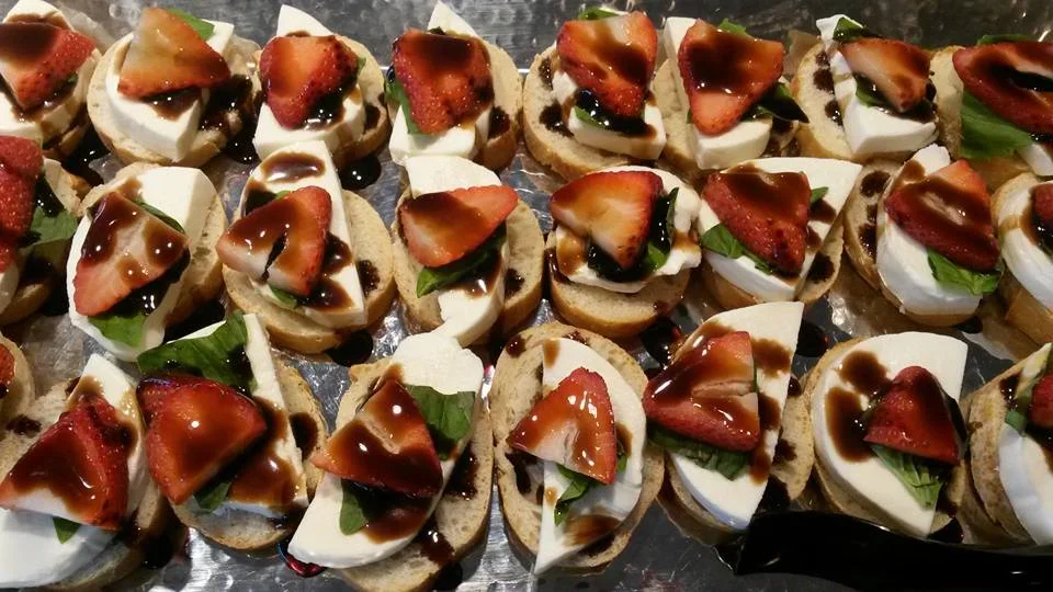 Assorted small bruschetta bites with mozzarella, strawberry slices, basil leaves, and balsamic glaze on toasted baguette slices.