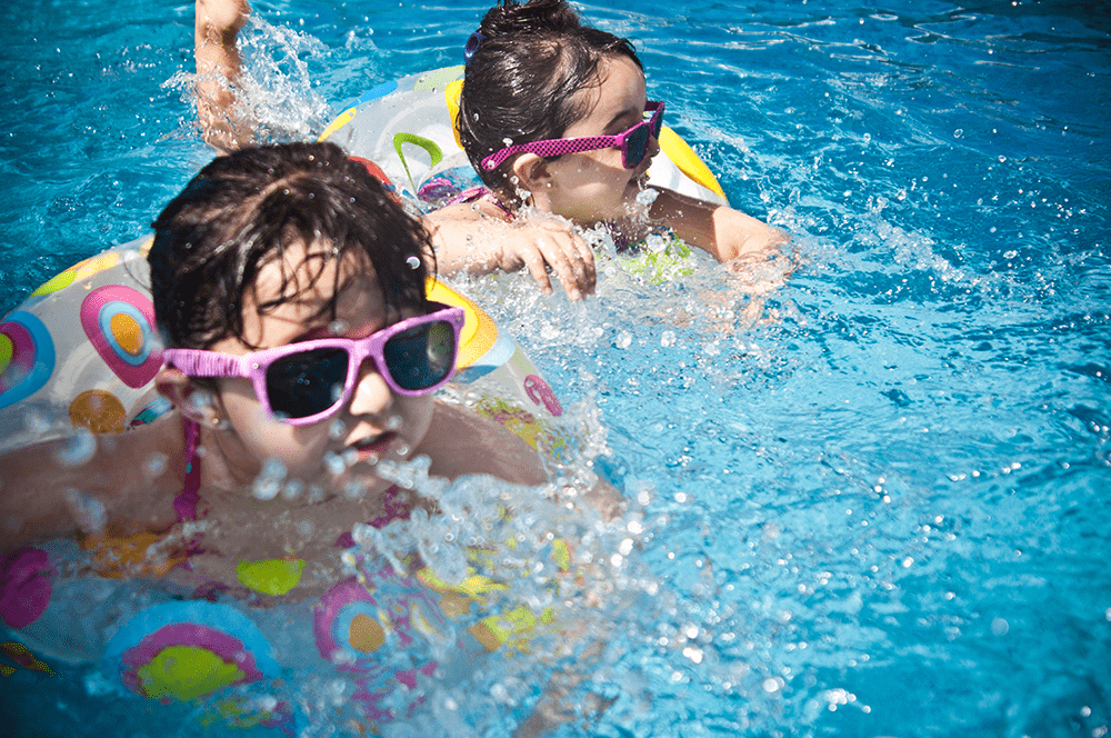 Two young girls swimming in a pool with inflatable rings, wearing sunglasses.