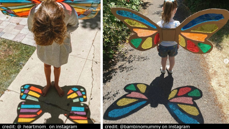 Two children standing on colorful chalk drawings of butterflies on a sidewalk, one with rainbow-colored wings and the other with multicolored wings, casting shadows.